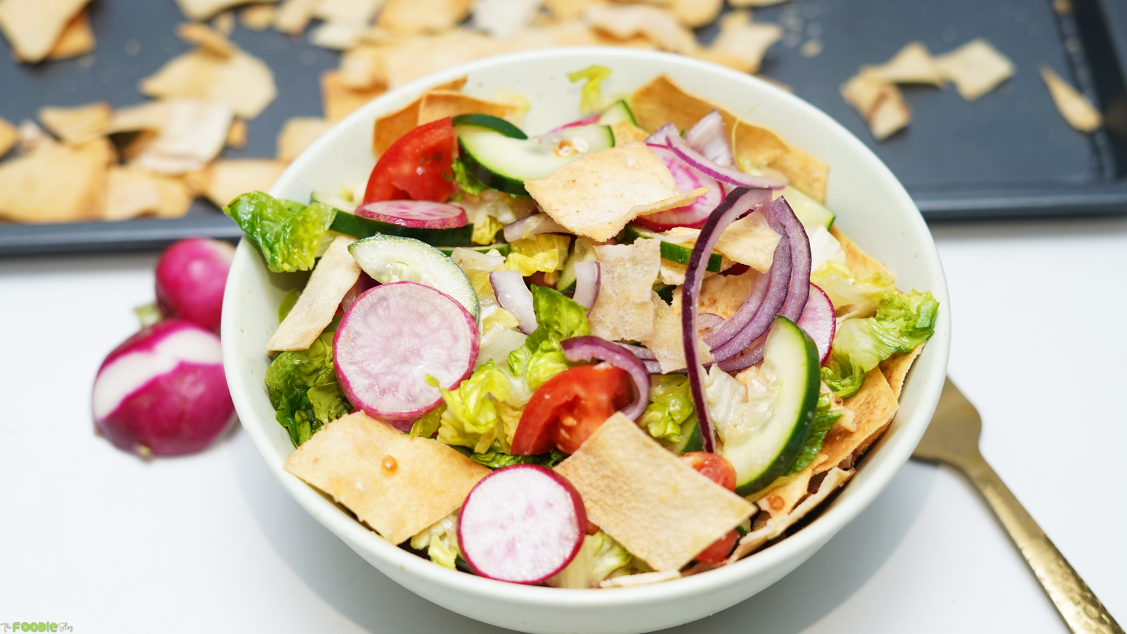 Bowl of Lebanese Fattoush Salad with romaine lettuce, cucumbers, tomatoes, radishes, red onion, and crispy pita bread pieces.