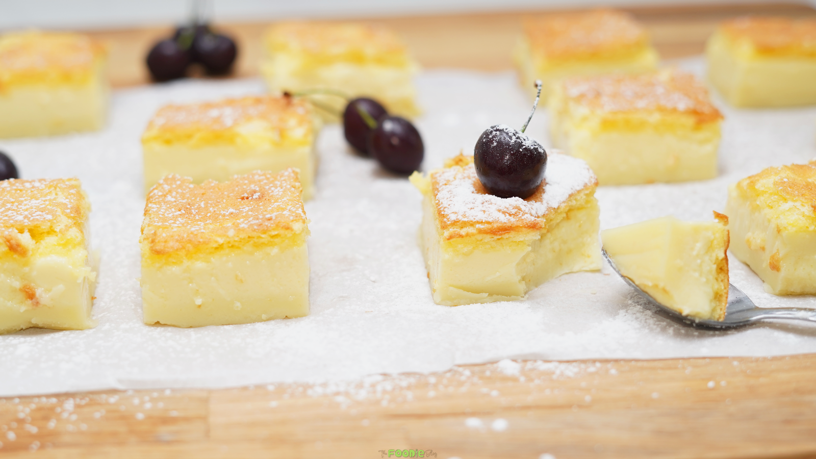 Magic Three Layer Custard Cake squares dusted with powdered sugar and topped with fresh cherries.