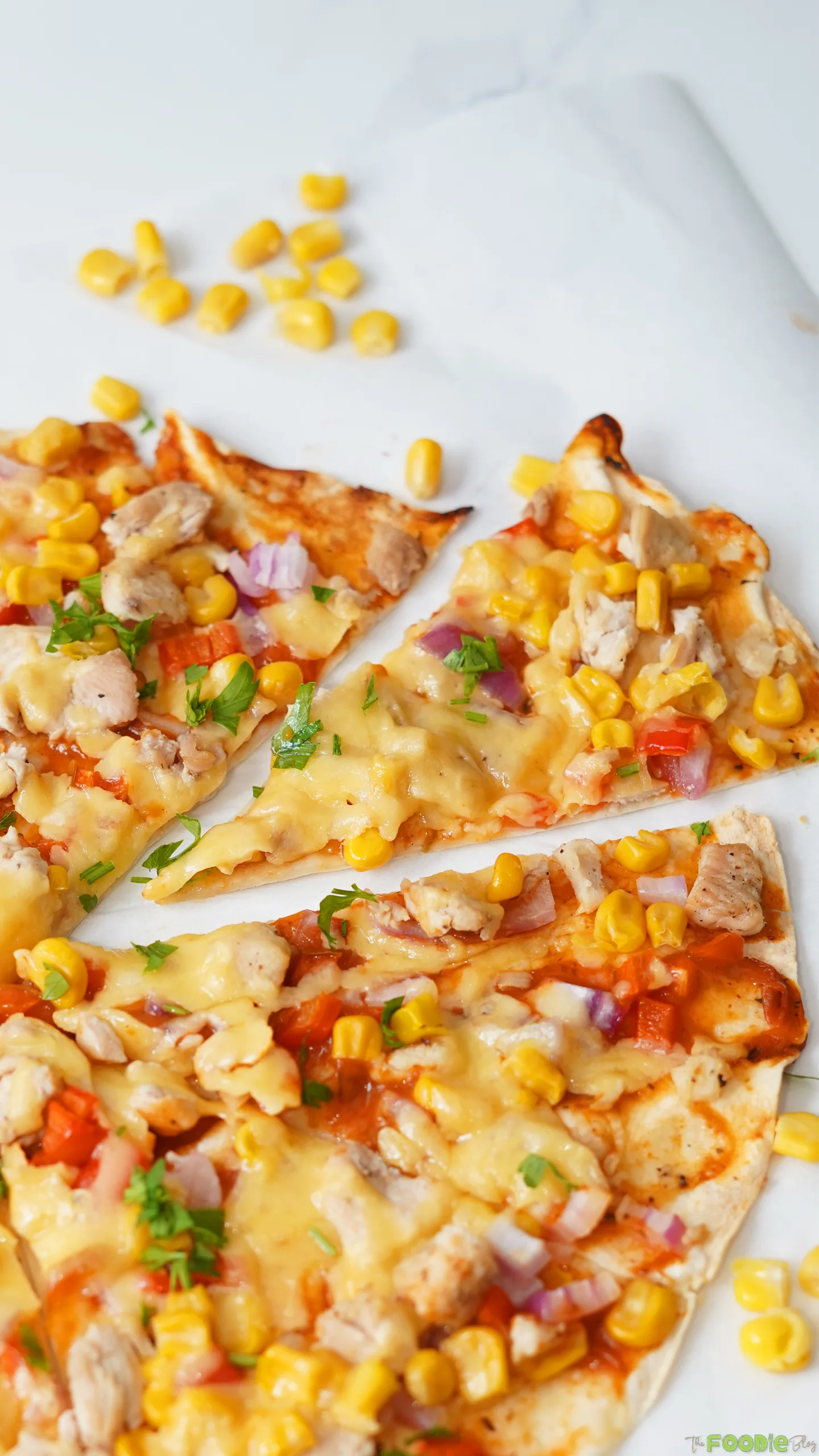 Sliced Mexican flatbread pizza wedges with chicken, corn, melted cheese, and red onion.