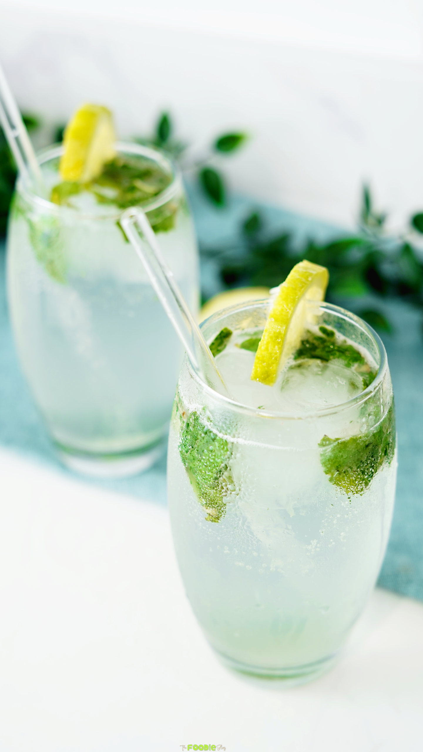 Close-up mojito cocktail with mint leaves, ice, lemon garnish, and a clear straw in a chilled glass.
