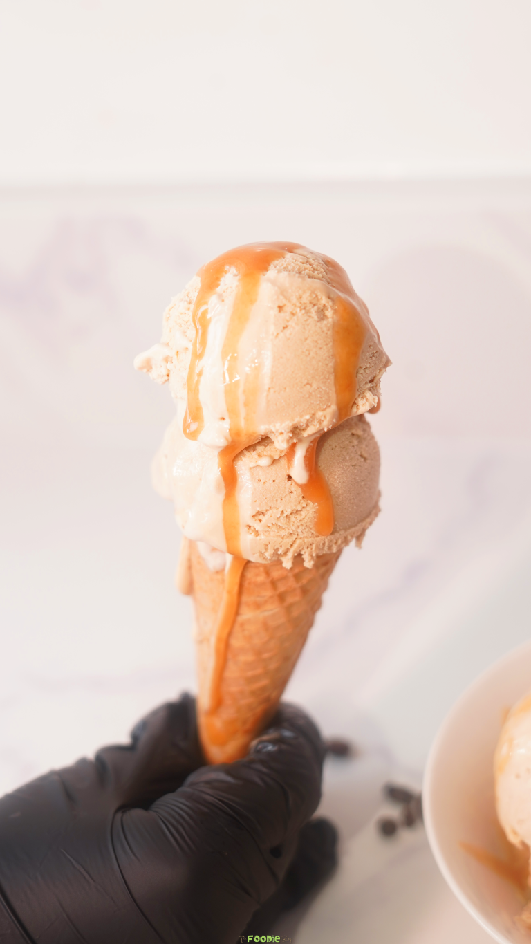 No-churn coffee ice cream in a waffle cone with coffee beans and caramel sauce.