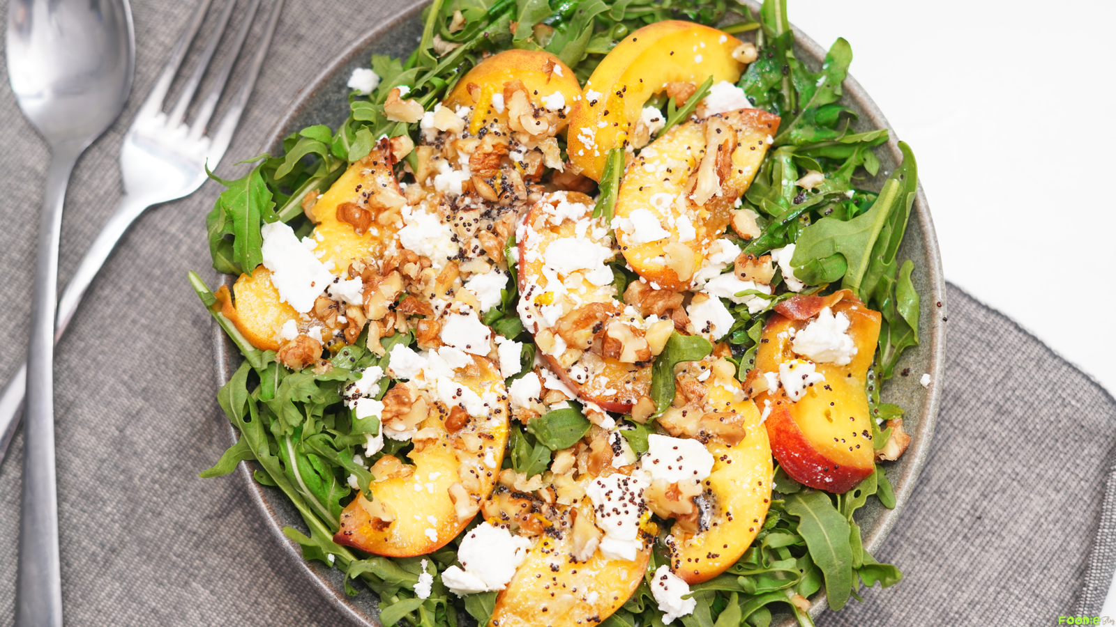 Fresh peach salad served on arugula with crumbled feta, chopped walnuts, and poppyseed dressing