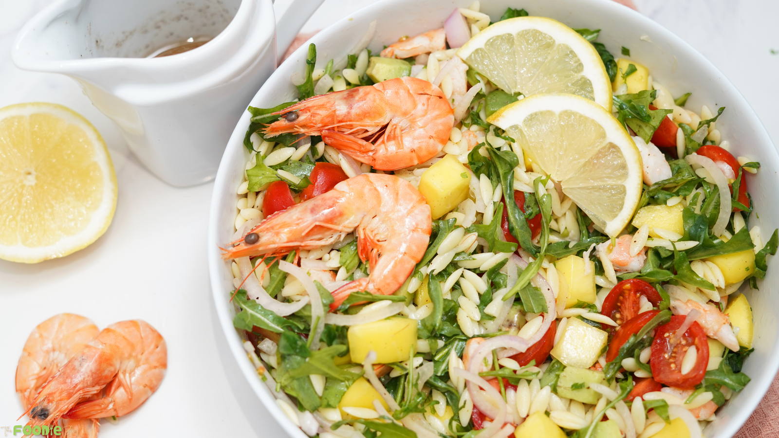 Close-up of prawn mango avocado summer salad with shrimp, orzo, mango cubes, avocado, arugula, cherry tomatoes, and lime dressing.