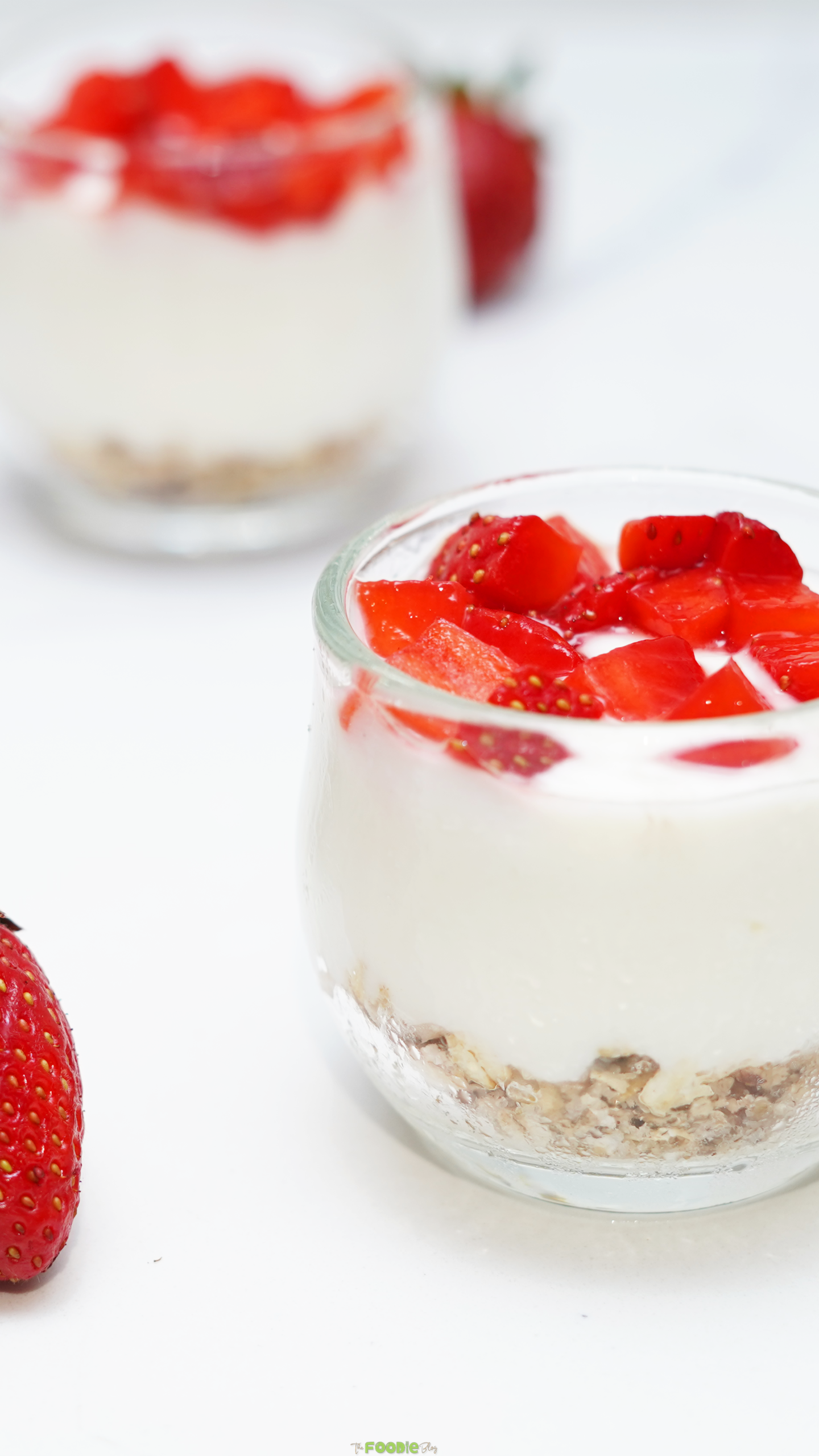 Close-up of a creamy no bake cheesecake cup with chopped strawberries on top and an oat crust layer at the bottom.