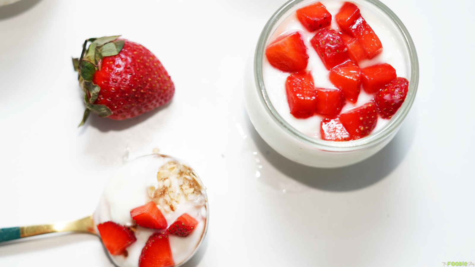 A spoonful of protein cheesecake with oat crust and strawberries beside a finished cheesecake cup.