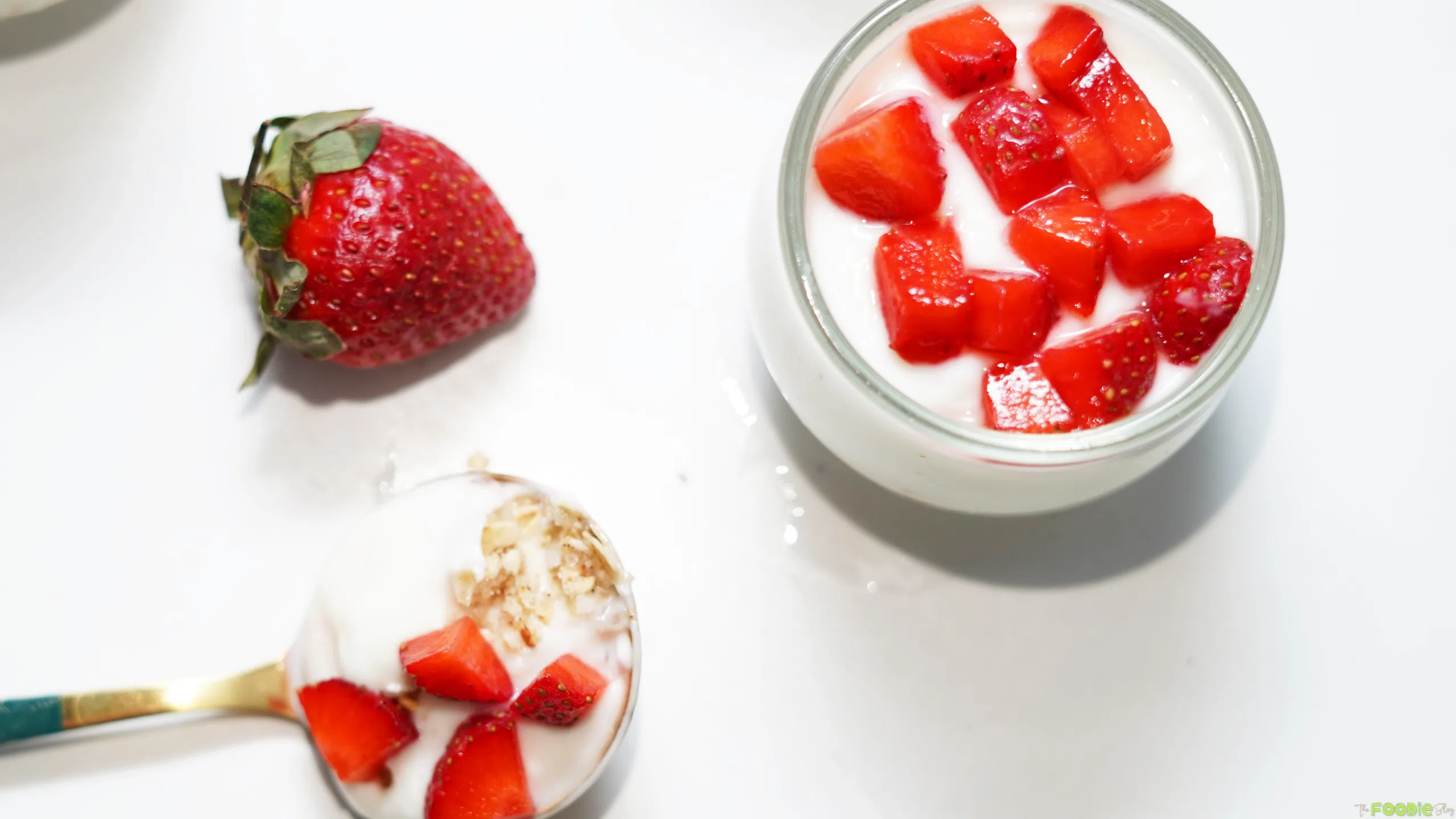 A spoonful of protein cheesecake with oat crust and strawberries beside a finished cheesecake cup.