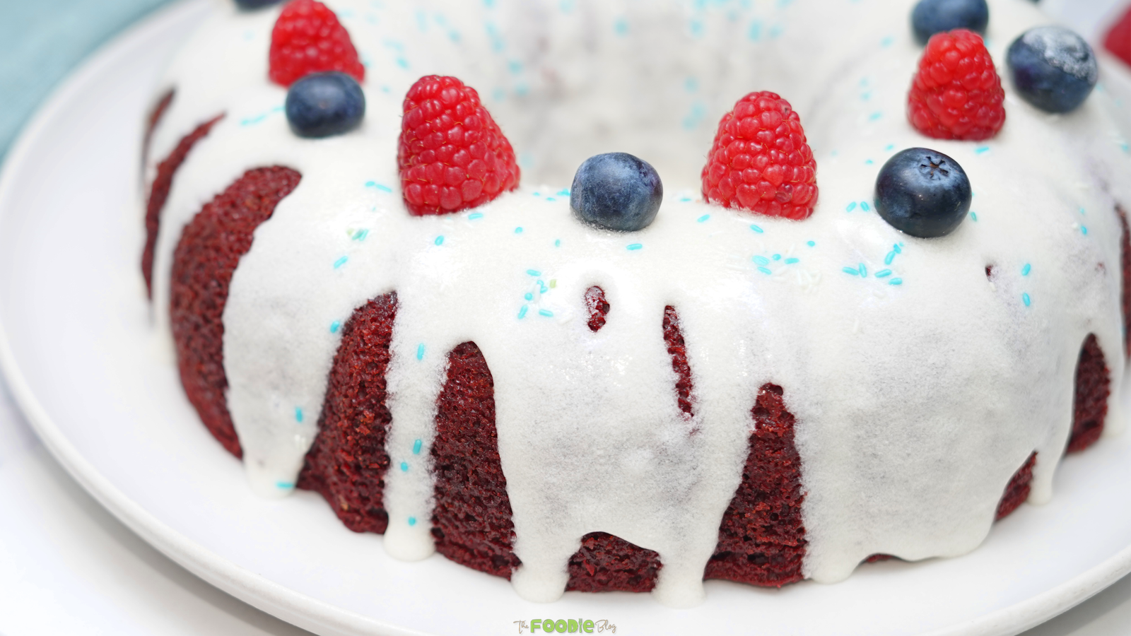 Red Velvet 4th of July Cake topped with cream cheese glaze, raspberries, blueberries, and blue sprinkles.
