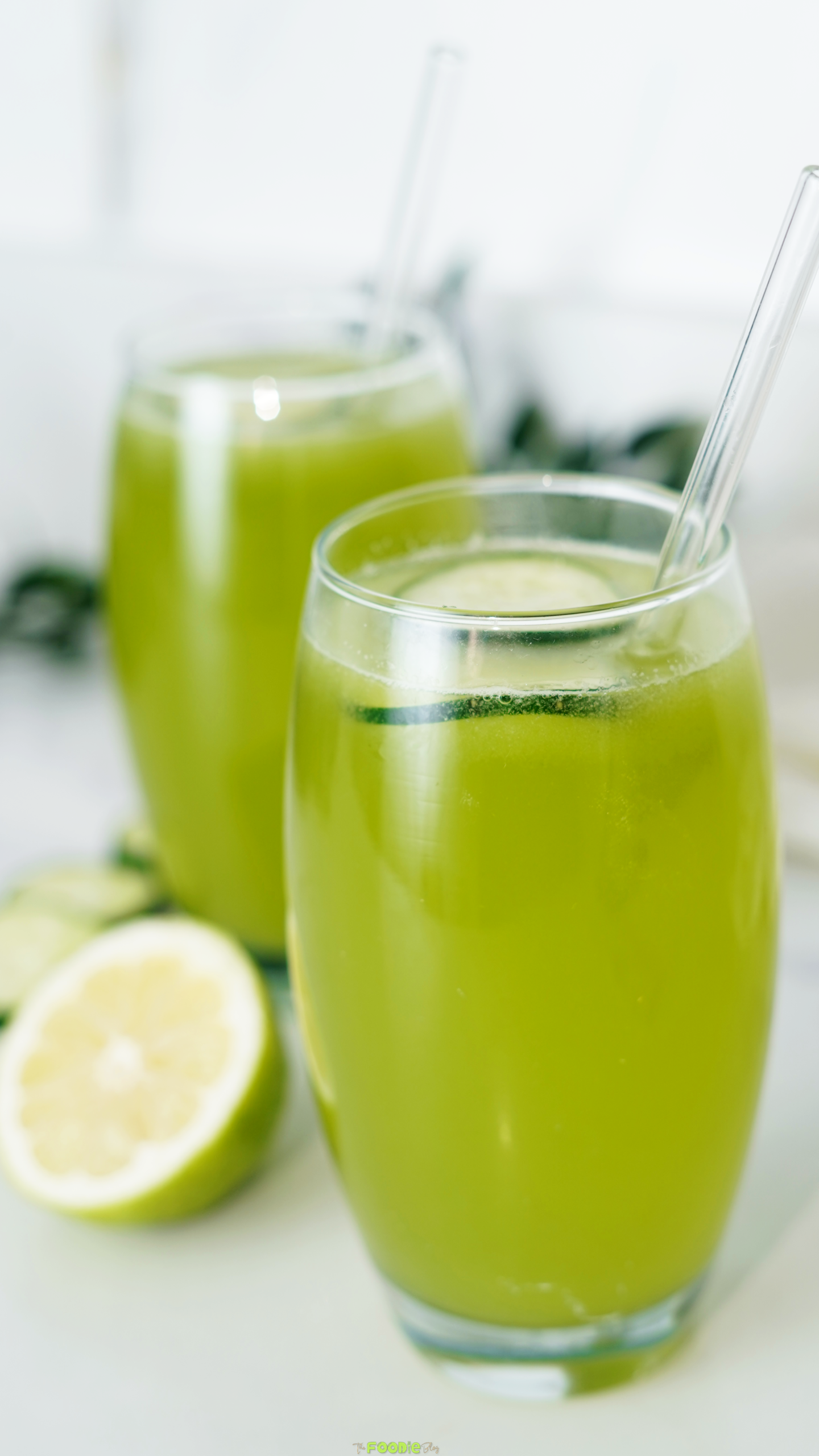 A chilled green cucumber and lemon drink in a clear glass with cucumber slices floating on top.