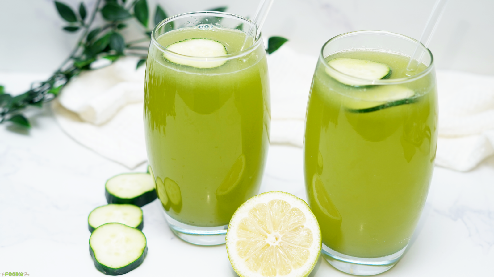 Two glasses of green cucumber lemonade garnished with cucumber slices and lemon.