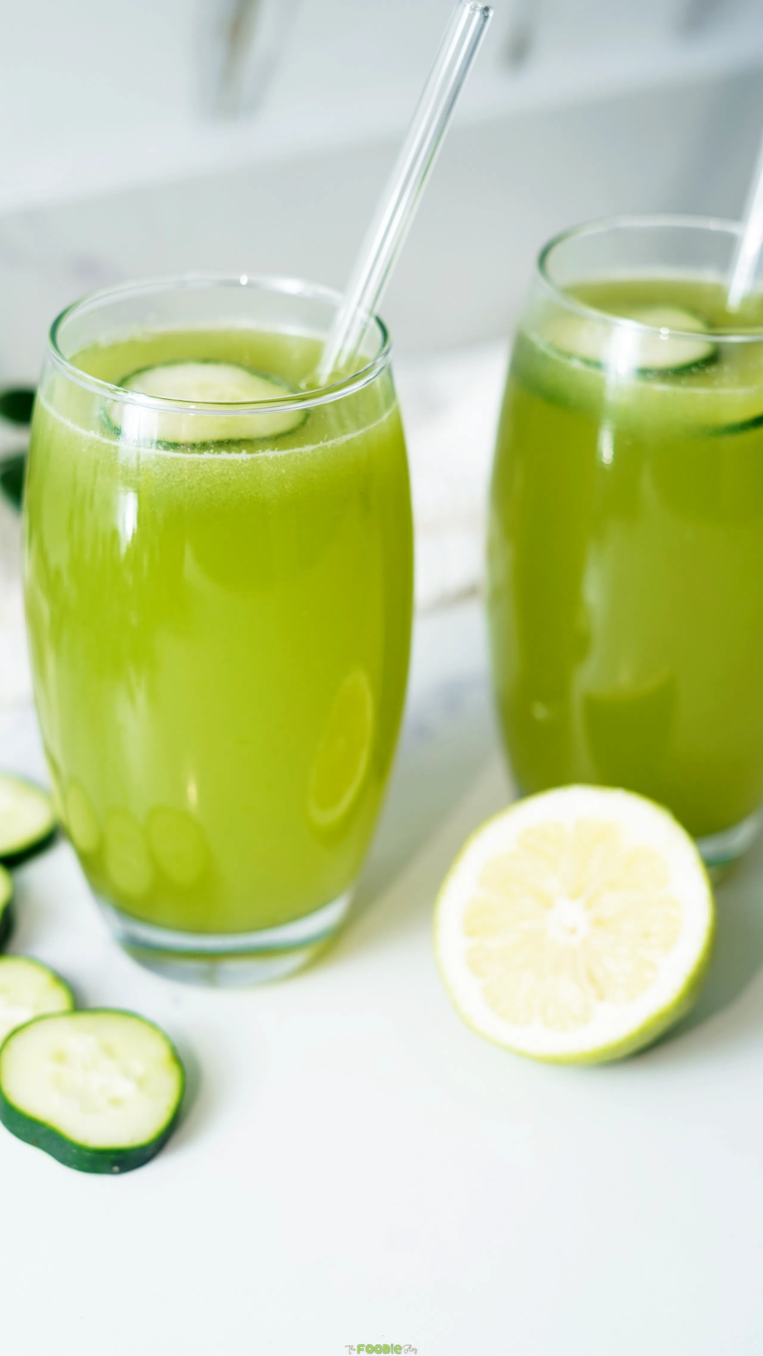 Two tall glasses of cucumber and lemon drink with fresh cucumber slices and a lemon half.