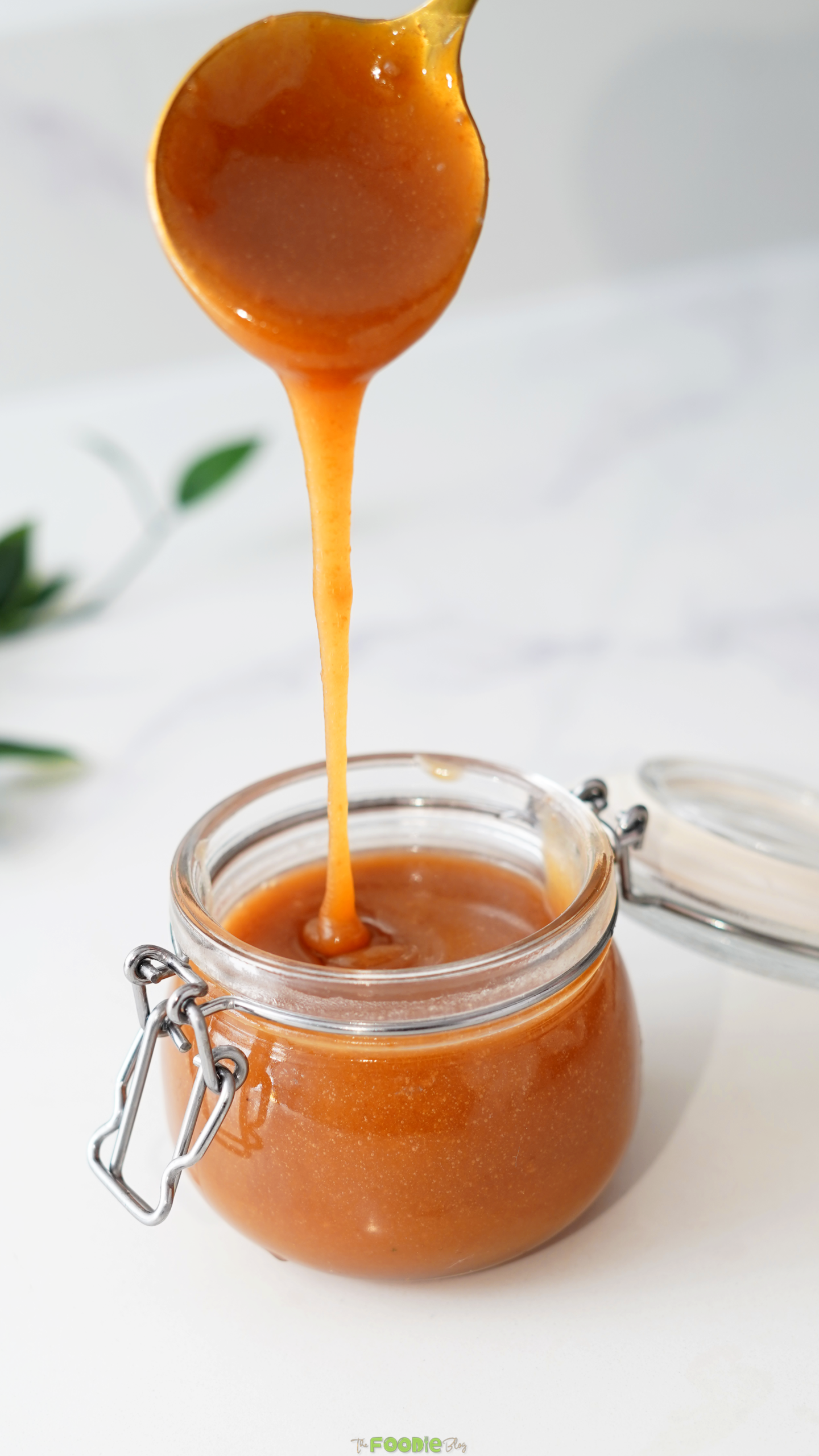 Salted caramel sauce dripping from a spoon into a small glass jar