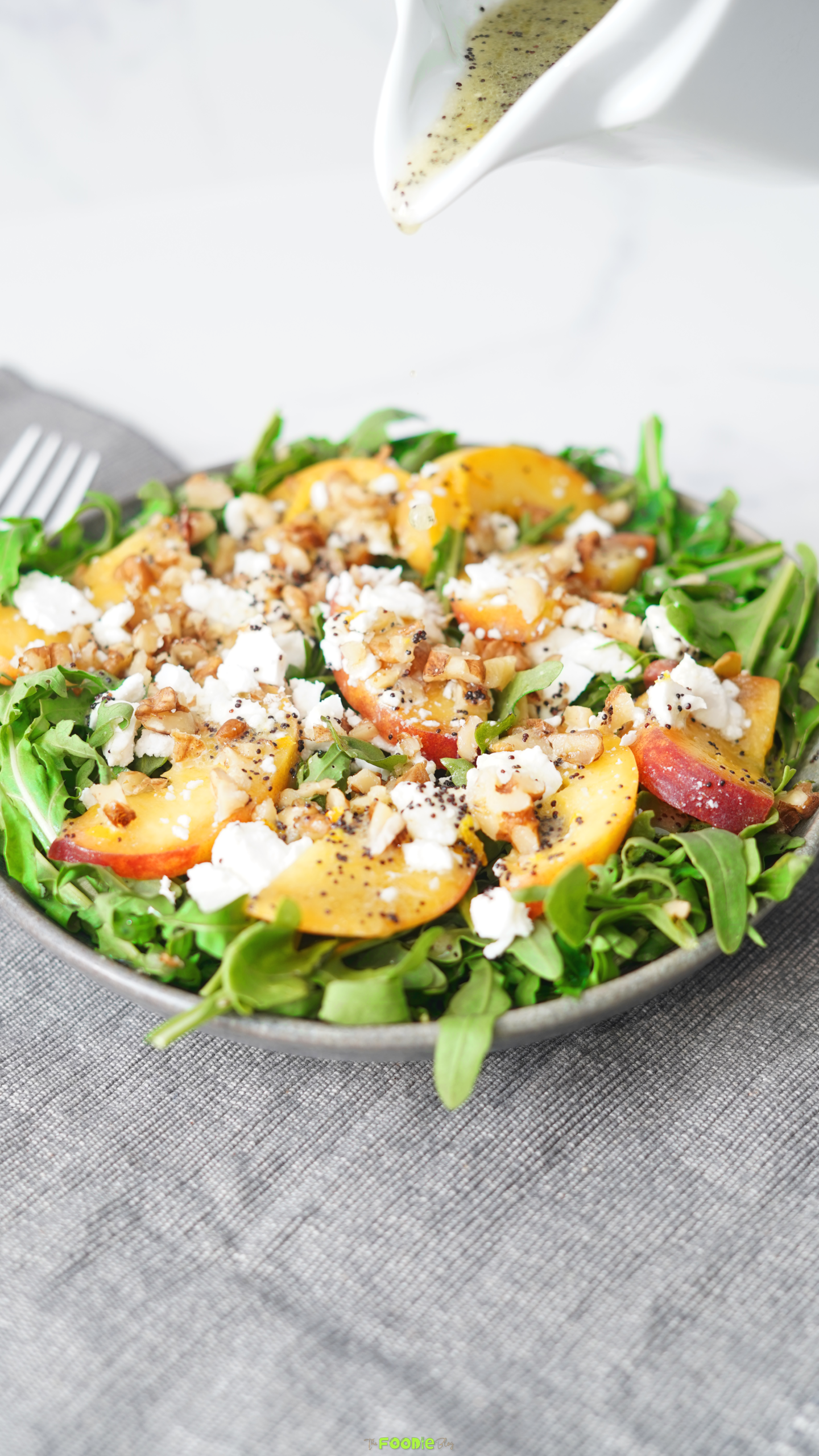 Summer peach salad with sliced peaches, arugula, crumbled feta, chopped walnuts, and poppyseed dressing.