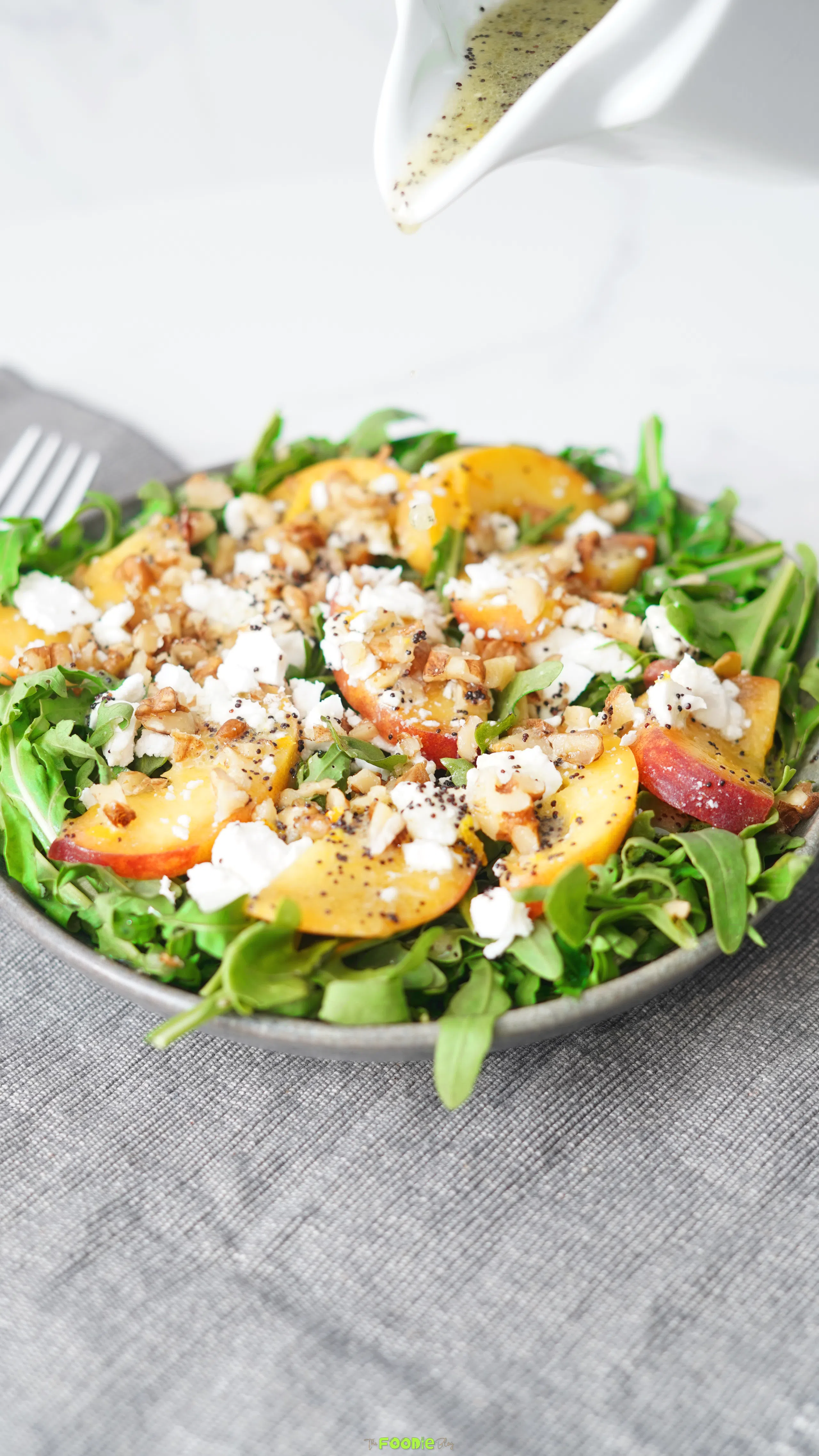 Summer peach salad with sliced peaches, arugula, crumbled feta, chopped walnuts, and poppyseed dressing.