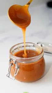 Thick golden caramel sauce falling from a spoon into a glass jar