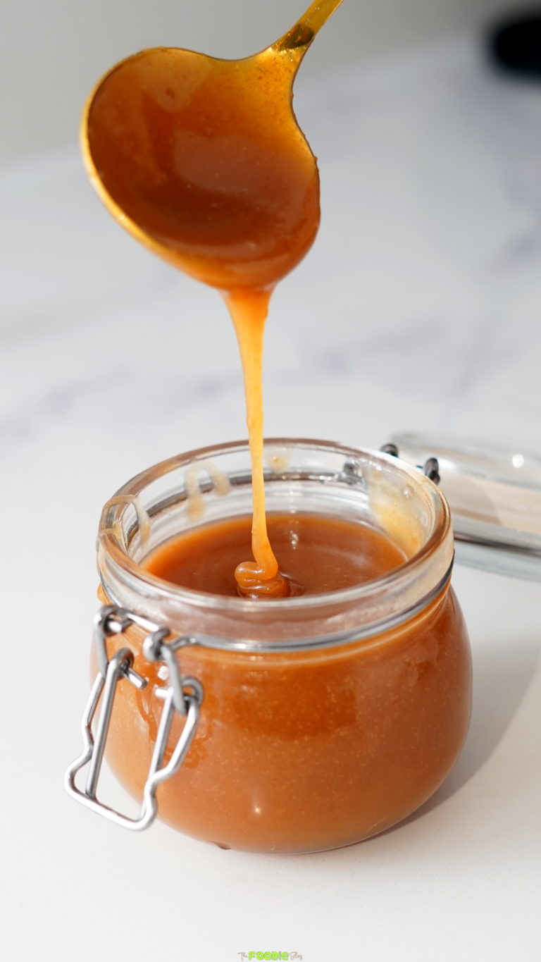 Thick golden caramel sauce falling from a spoon into a glass jar
