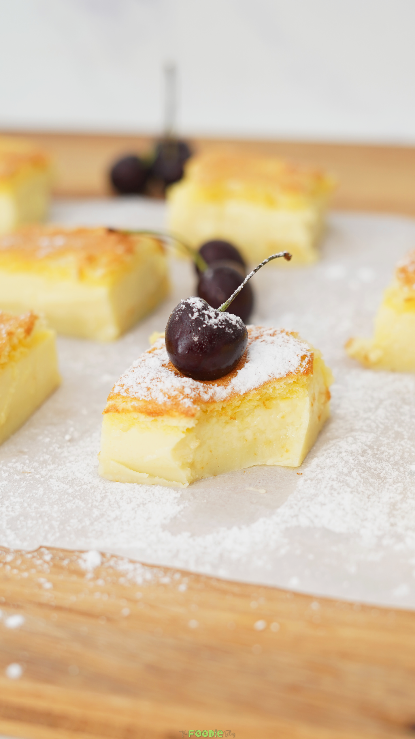 Close-up of a soft vanilla custard cake square with powdered sugar and a cherry.