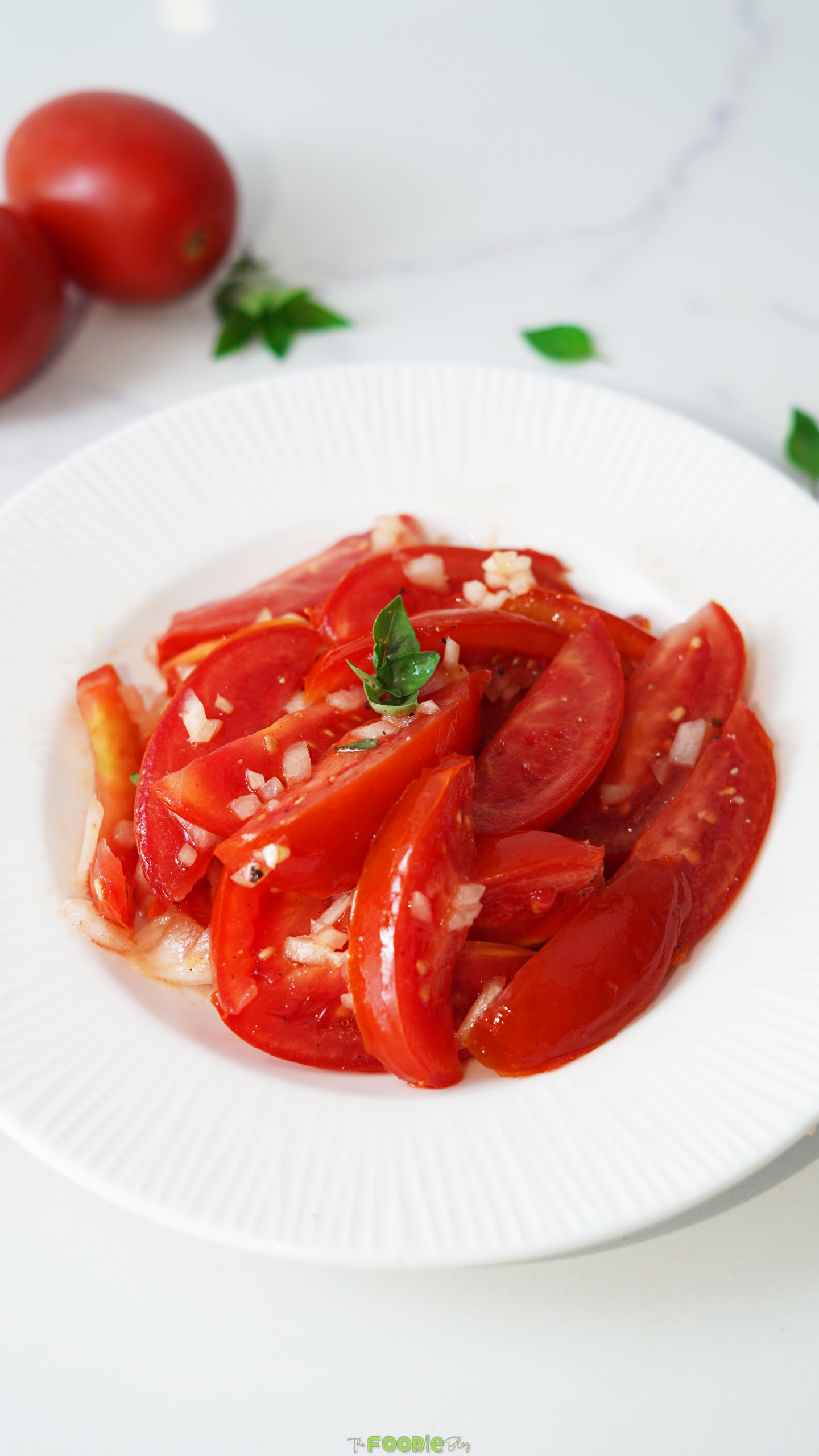 Tomato salad with basil, garlic, shallots, olive oil, and white wine vinegar served in a white bowl.