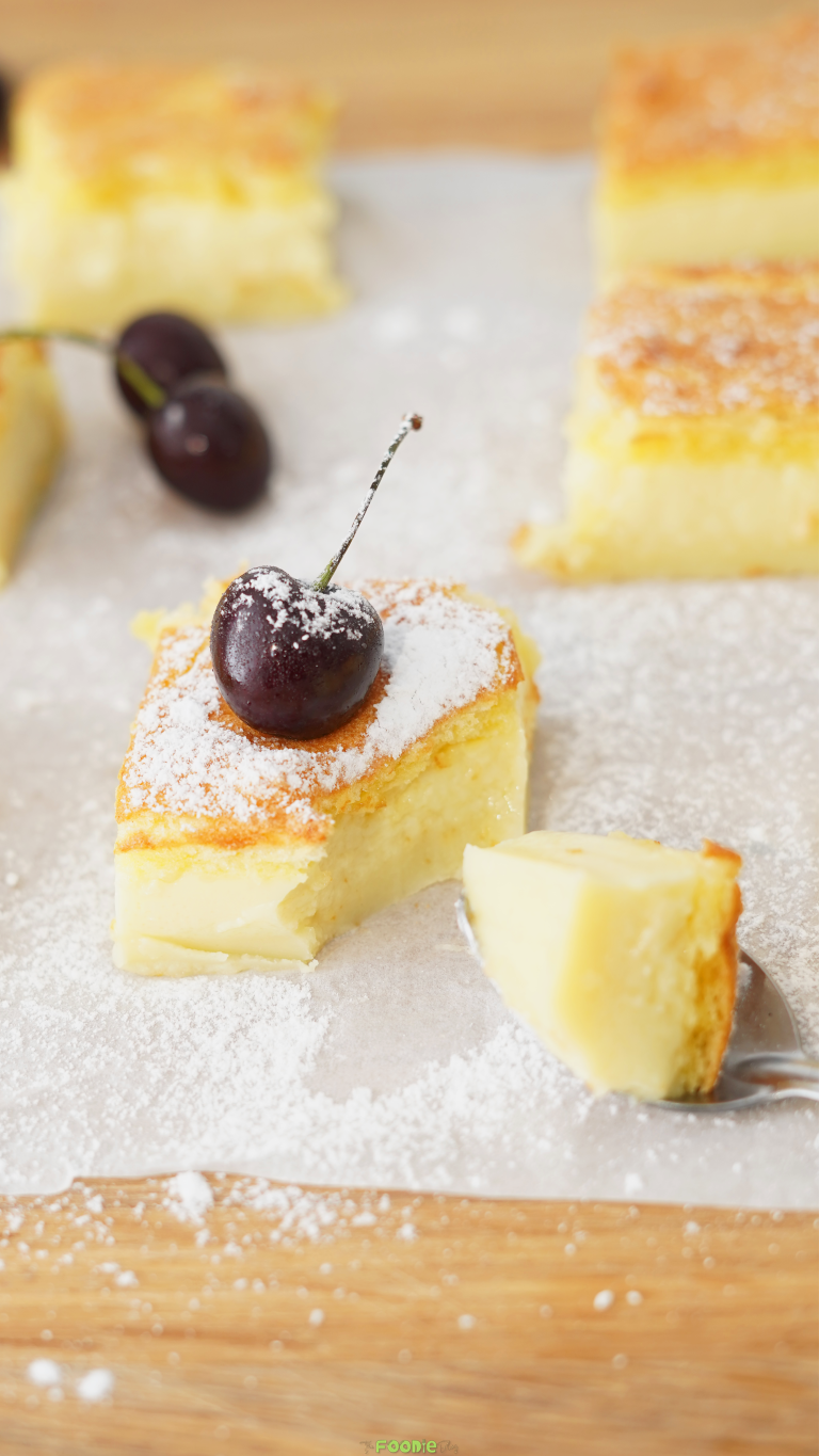 Vanilla custard cake square dusted with powdered sugar and topped with a fresh cherry.