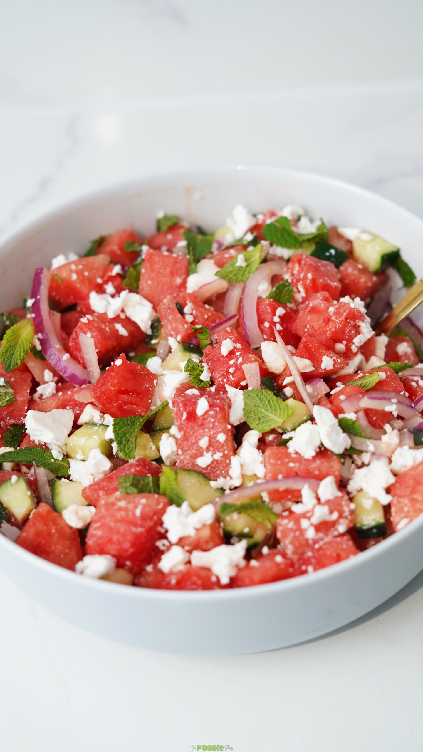 Final watermelon feta salad in a white bowl with watermelon cubes, cucumber, red onion, mint, and feta cheese.
