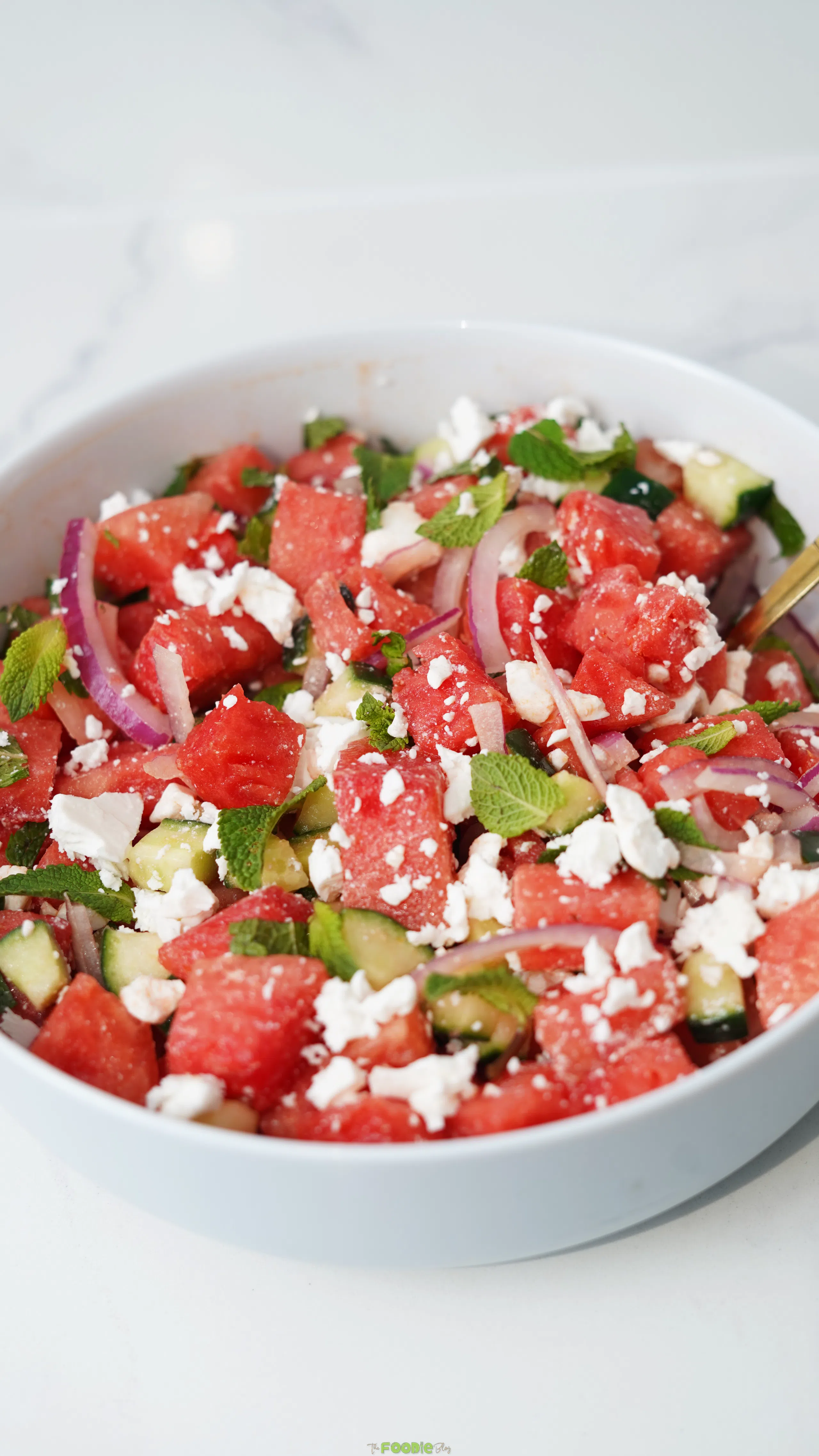 Final watermelon feta salad in a white bowl with watermelon cubes, cucumber, red onion, mint, and feta cheese.