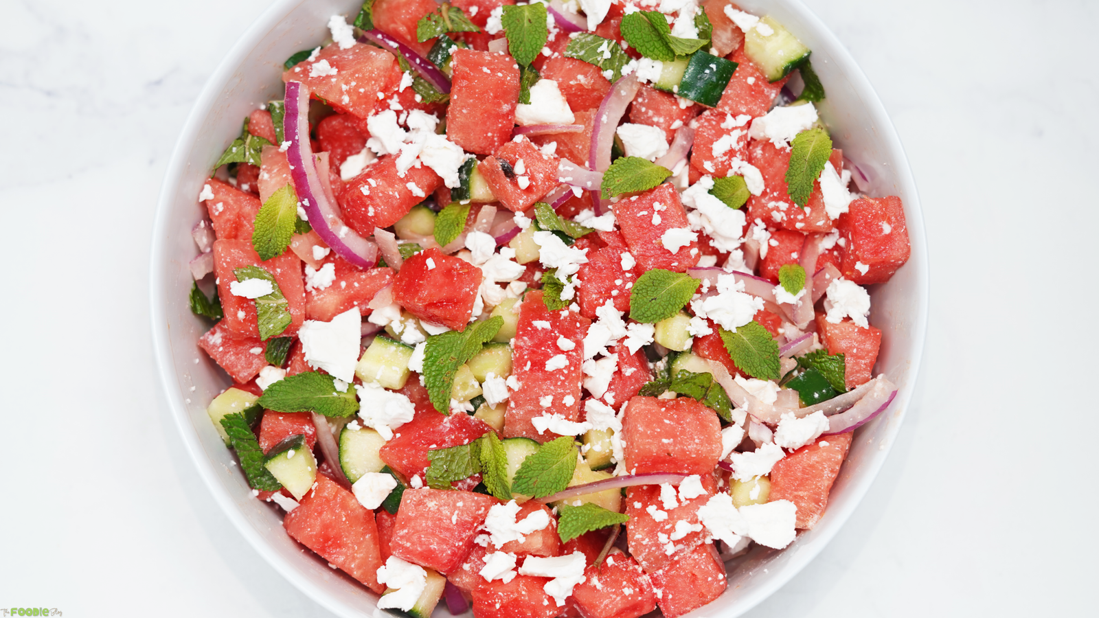 Watermelon feta salad served in a white bowl with cucumber, red onion, fresh mint, and crumbled feta cheese.