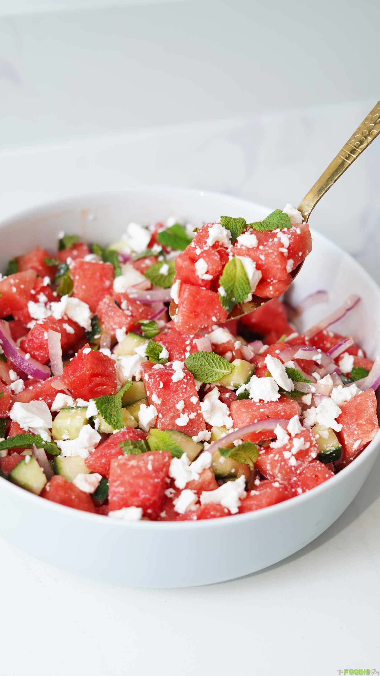 A spoon serving watermelon feta salad with mint, cucumber, red onion, and crumbled feta cheese.