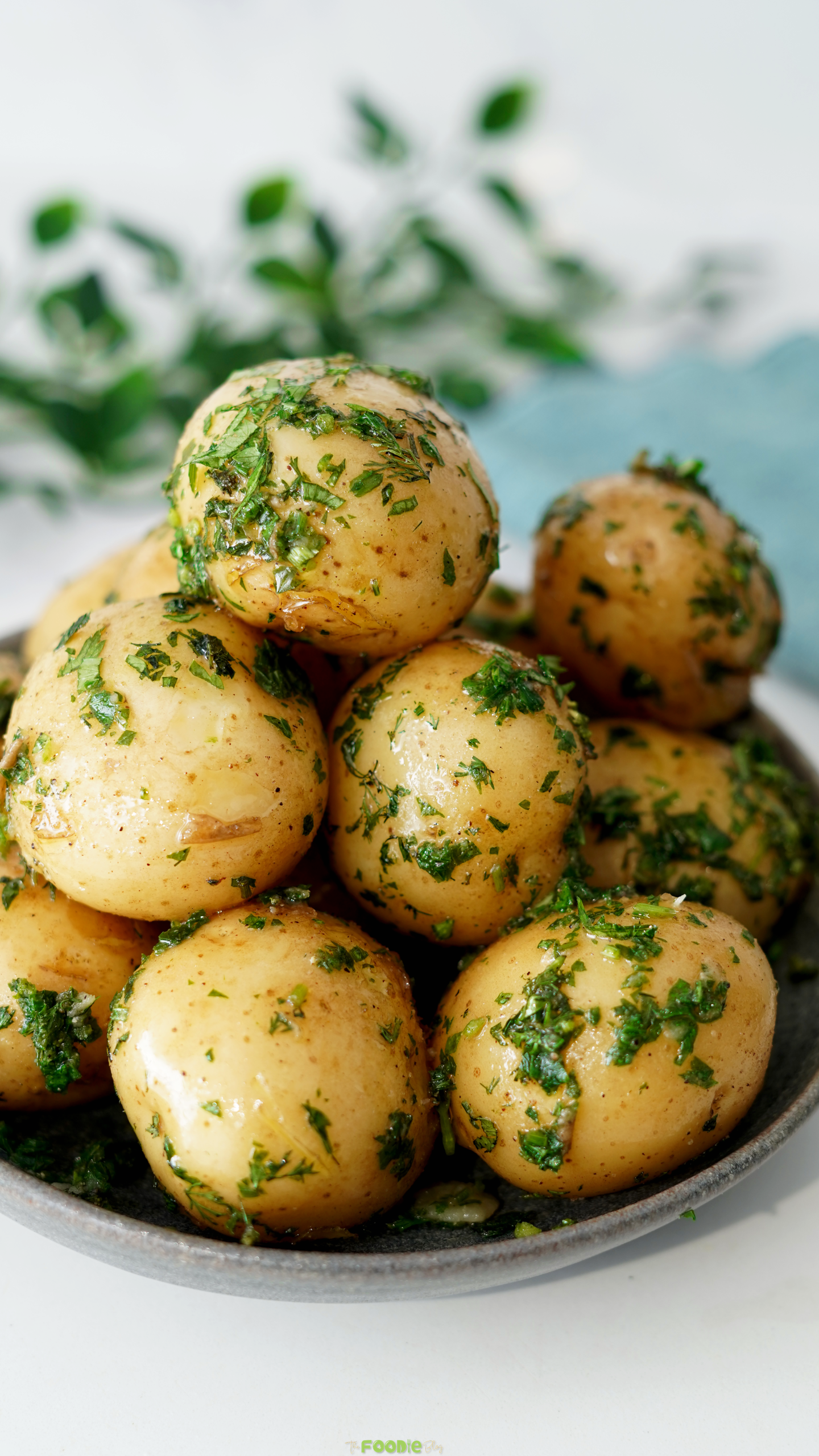 Tender baby potatoes tossed with butter, dill, chives, parsley, and black pepper in a serving bowl.