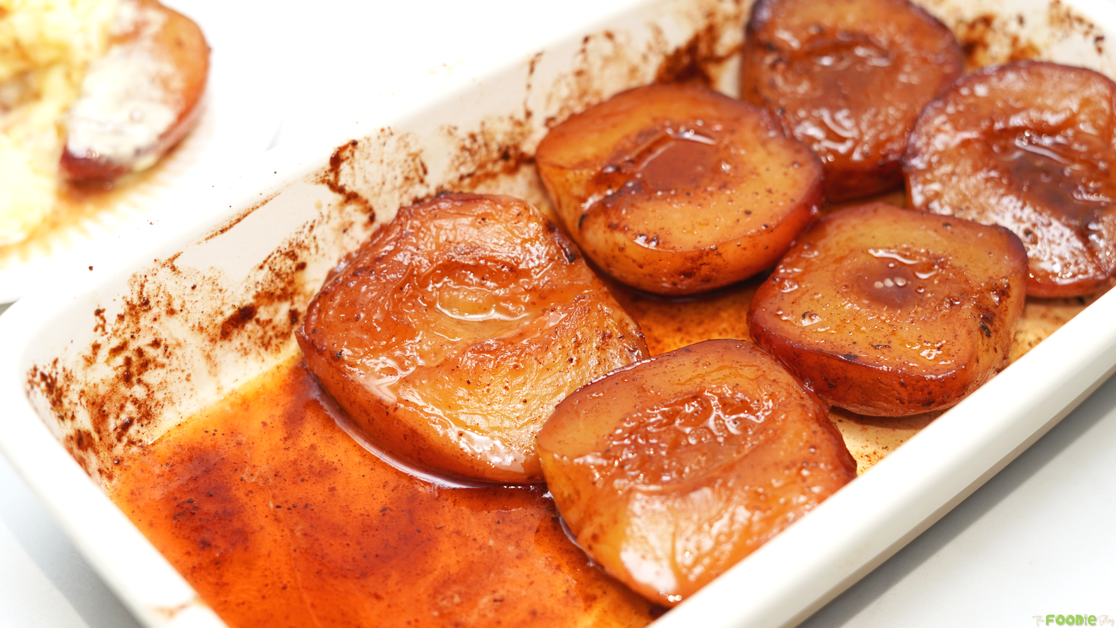 Baked peaches with honey, cinnamon, and nutmeg in a white baking dish.