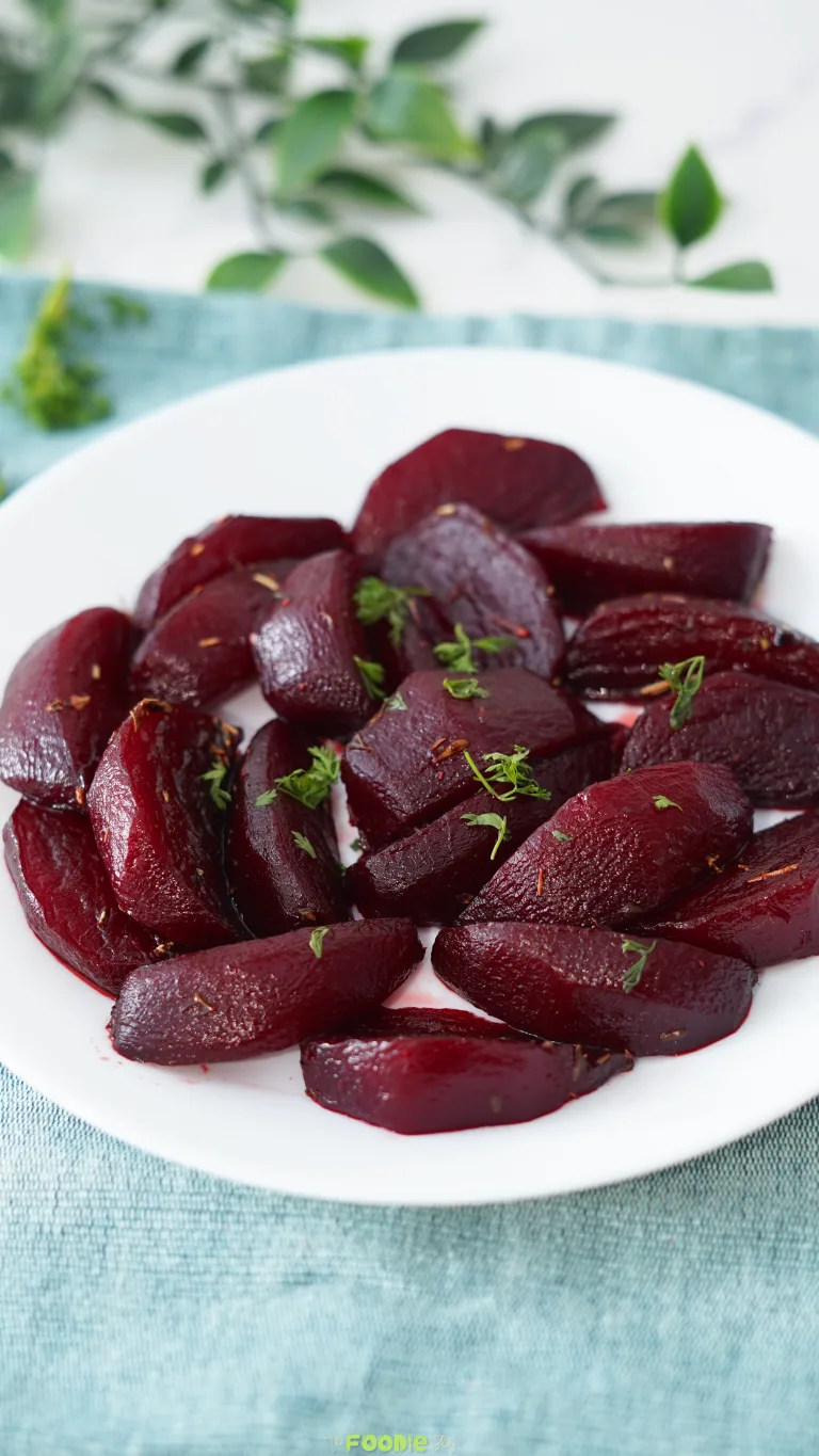 Balsamic Glazed Beetroot side dish served on a white plate with herbs over a blue cloth.