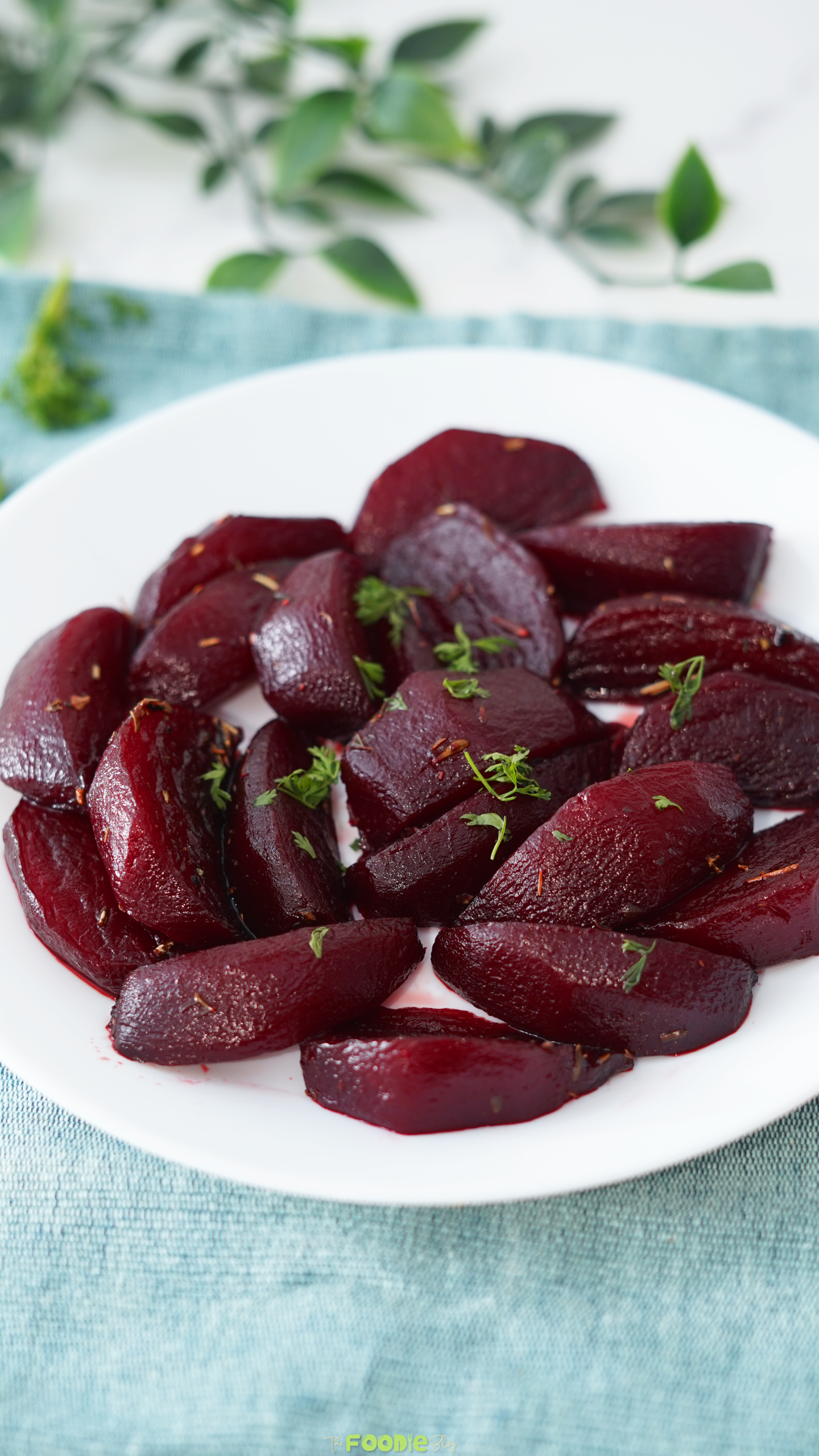 Balsamic Glazed Beetroot side dish served on a white plate with herbs over a blue cloth.