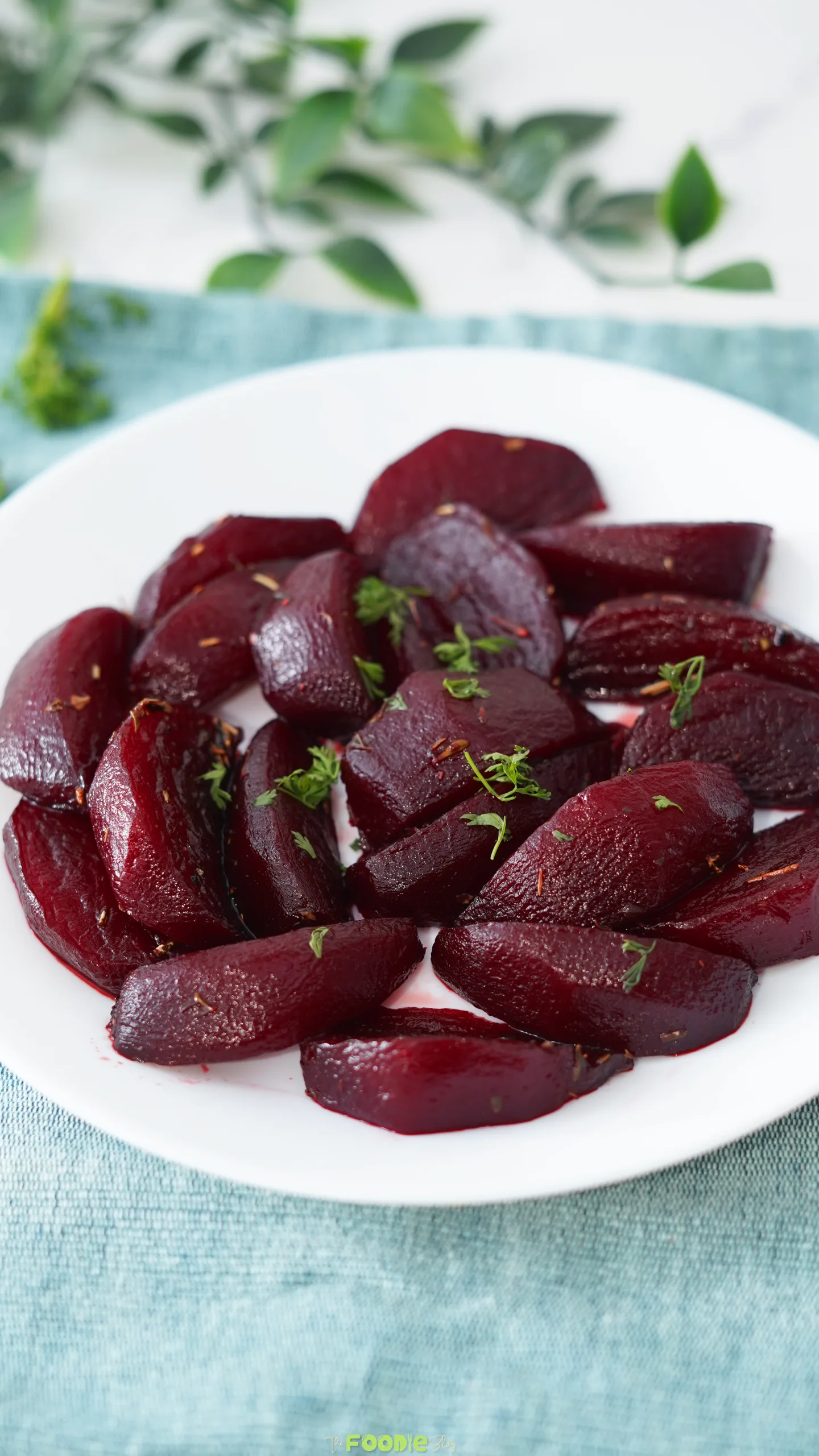 Balsamic Glazed Beetroot side dish served on a white plate with herbs over a blue cloth.