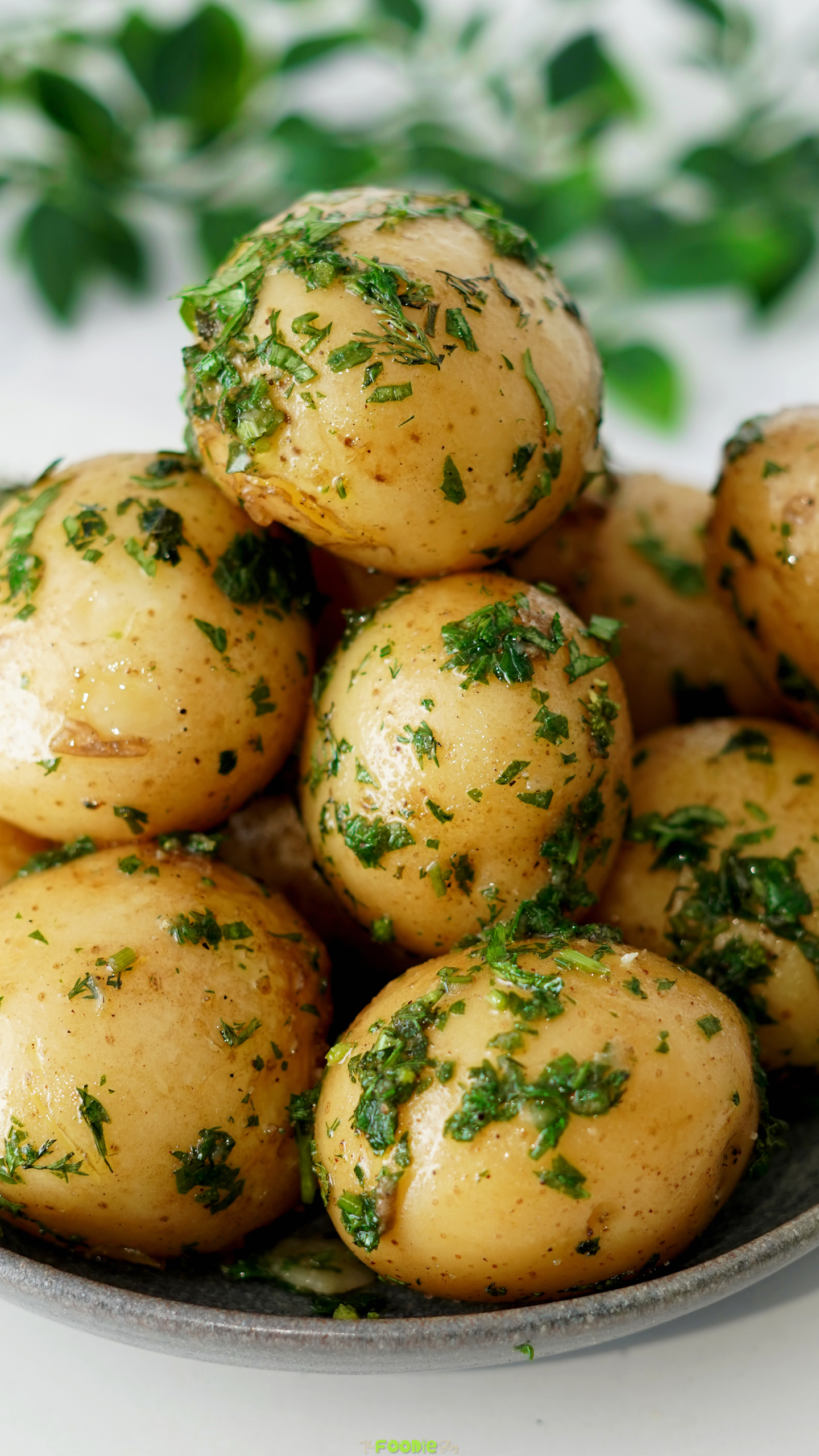 Close-up of glossy baby potatoes coated in butter and fresh green herbs.