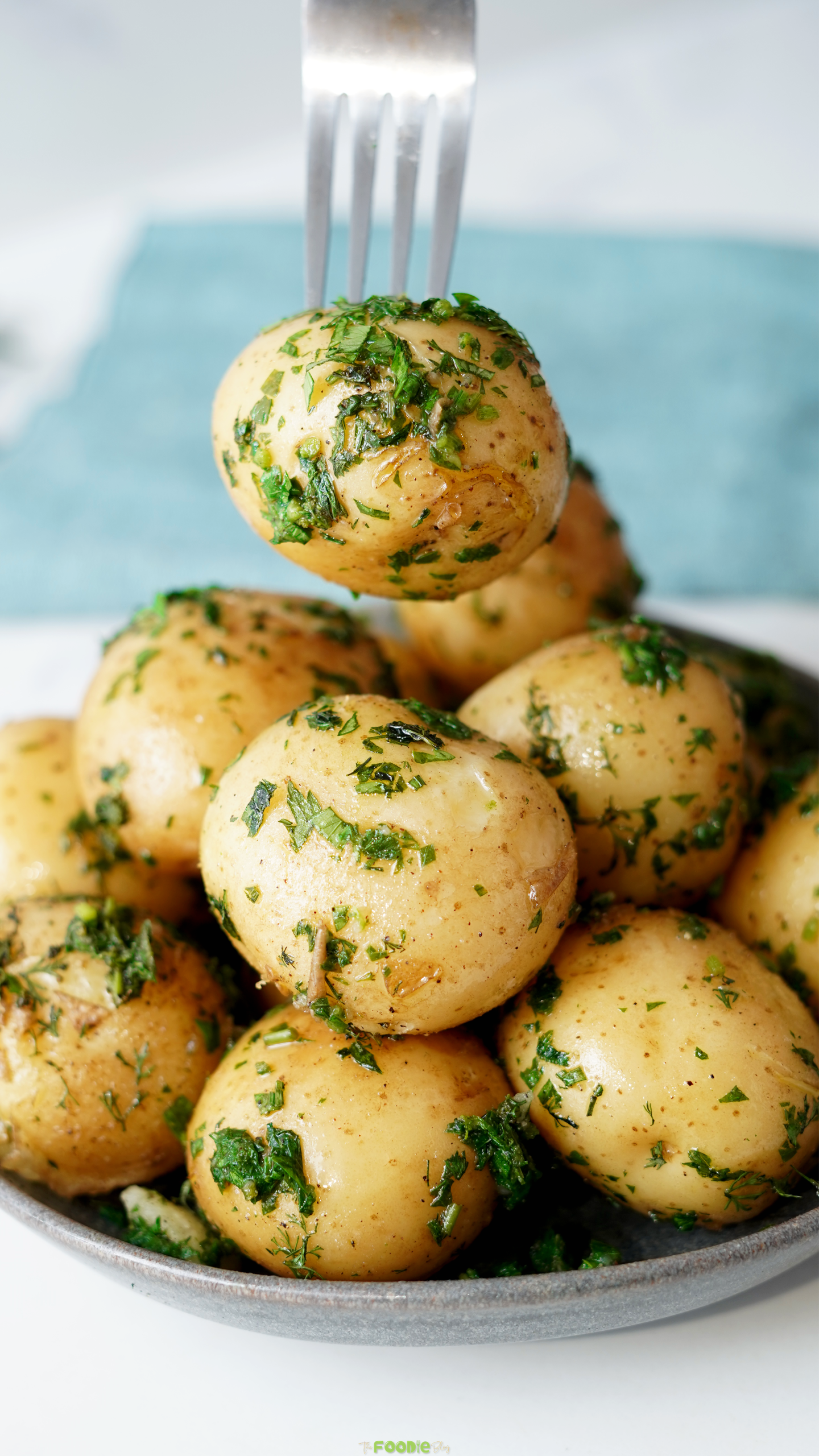 Fork lifting a tender baby potato coated in butter, dill, parsley, and chives.