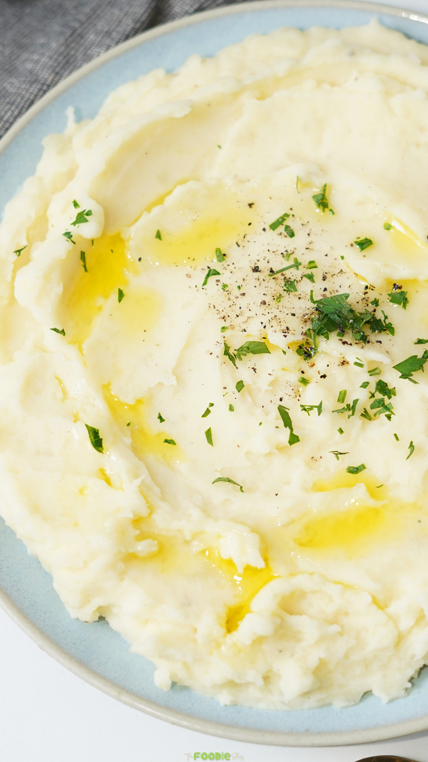 Close-up of buttery mashed potatoes with herbs, black pepper, and melted butter on top.
