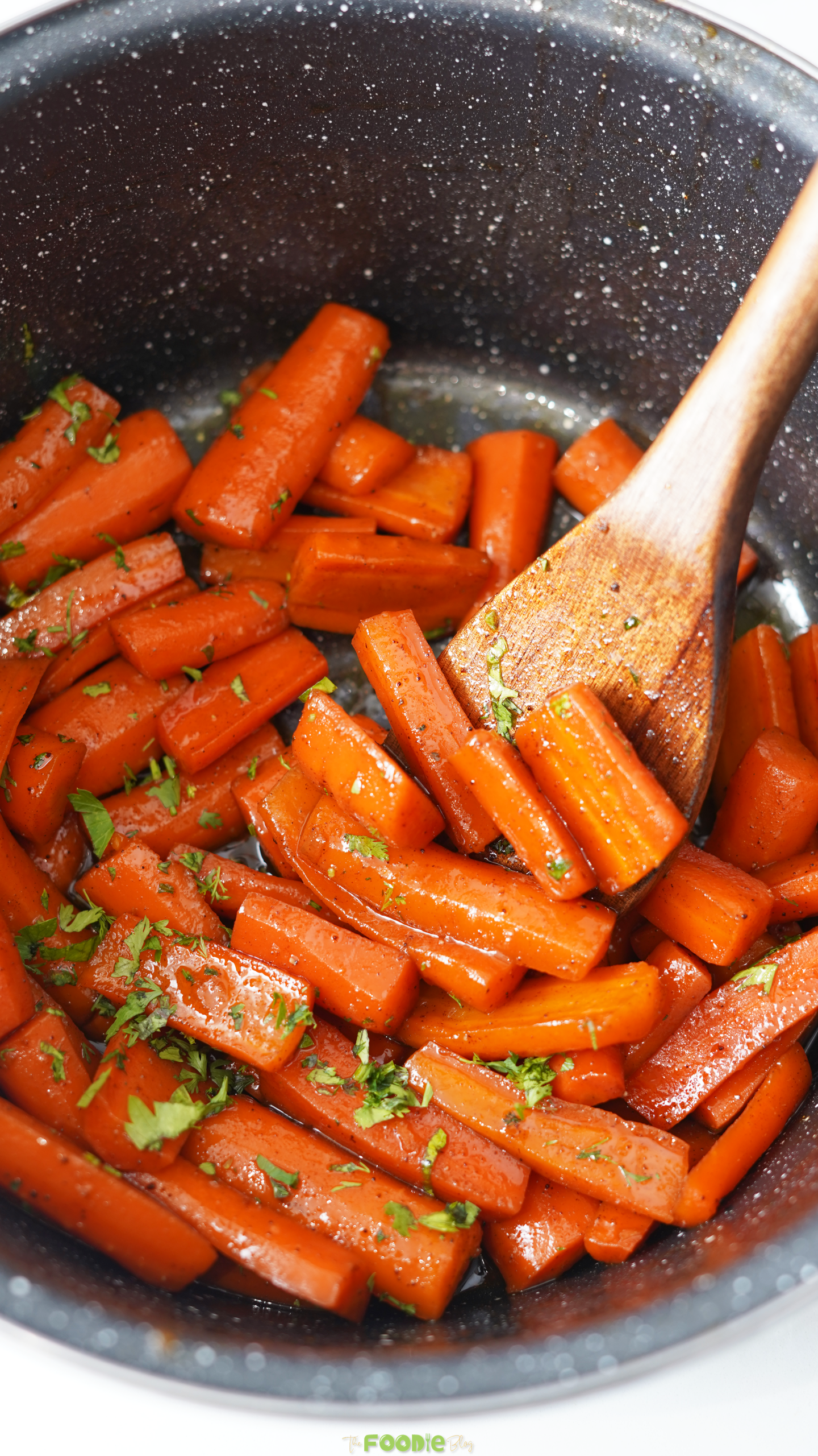 Candied carrots in a pot with a glossy butter brown sugar glaze and chopped parsley.