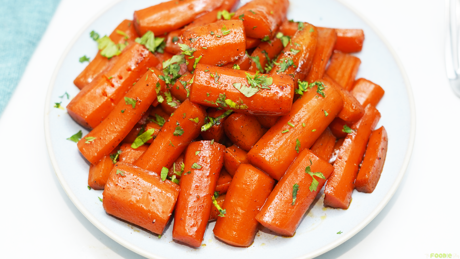 Candied carrots served on a plate with a glossy brown sugar butter glaze and chopped parsley.