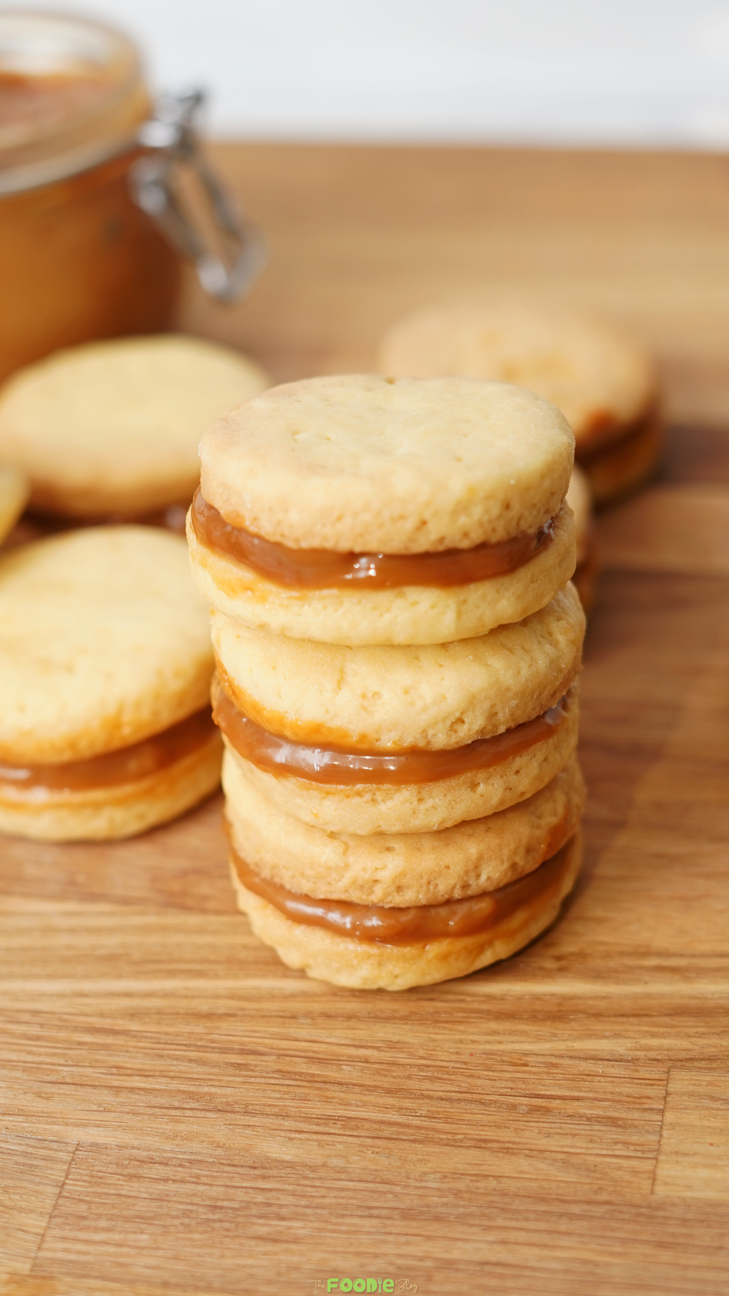Stacked shortbread cookie sandwiches with dulce de leche filling on a wooden board.