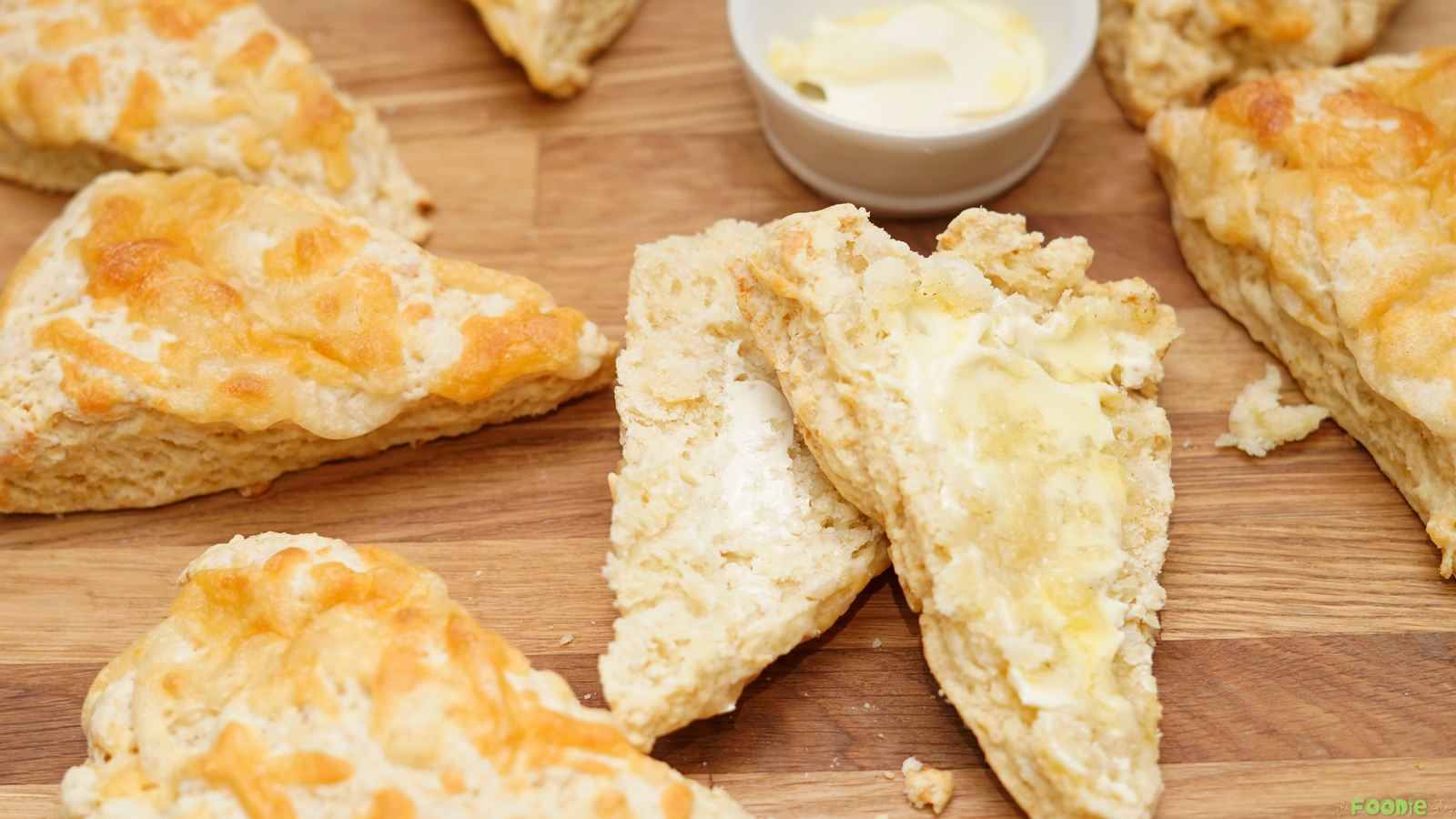 Freshly baked Cheese Scones split open and served warm with butter on a wooden board.