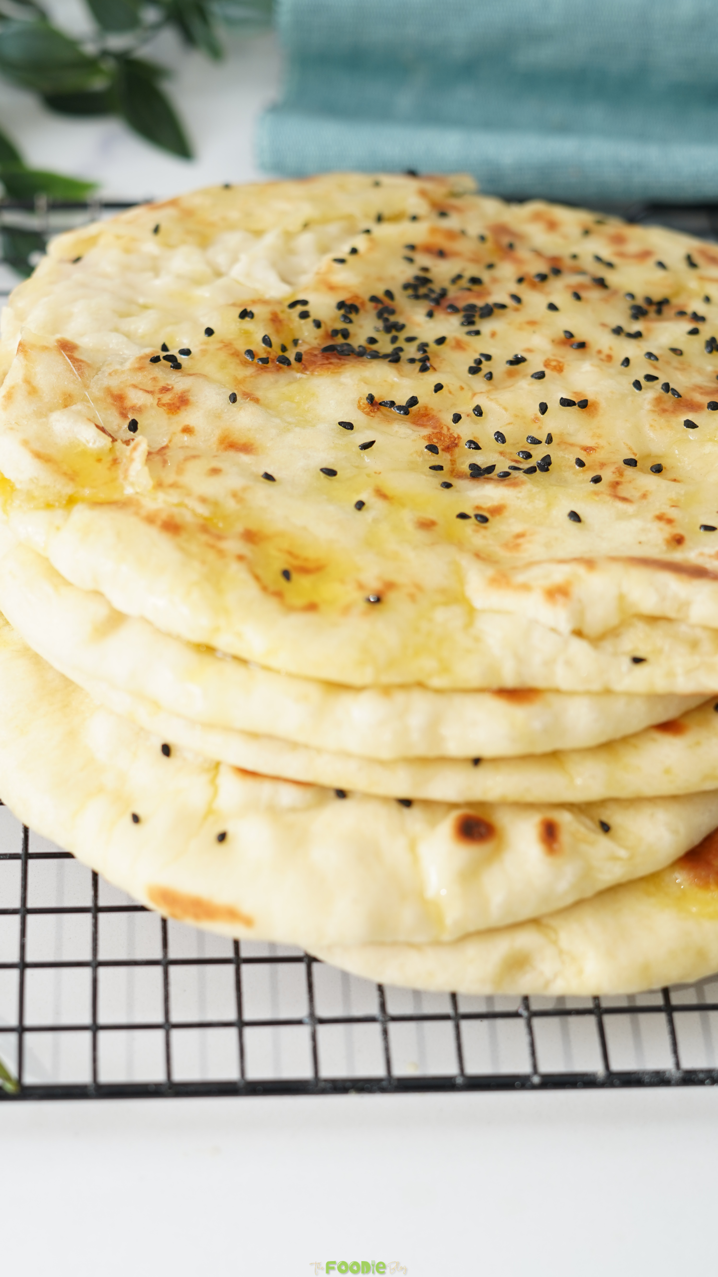 Stack of homemade cheese naan flatbreads cooling on a rack with black sesame seeds and melted butter.