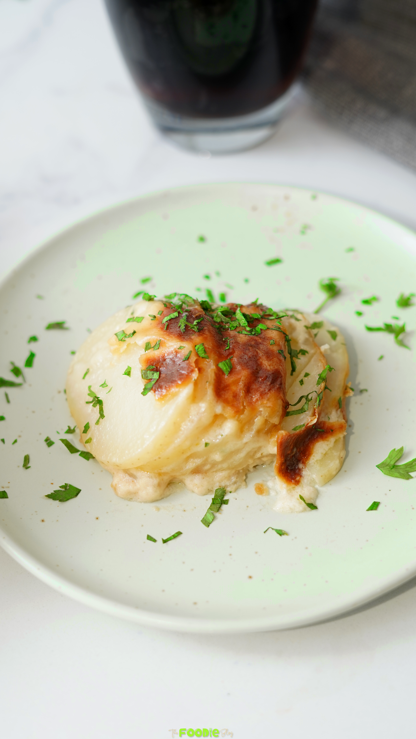 A serving of Cheesy Scalloped Potatoes on a plate with golden melted cheese and fresh parsley.