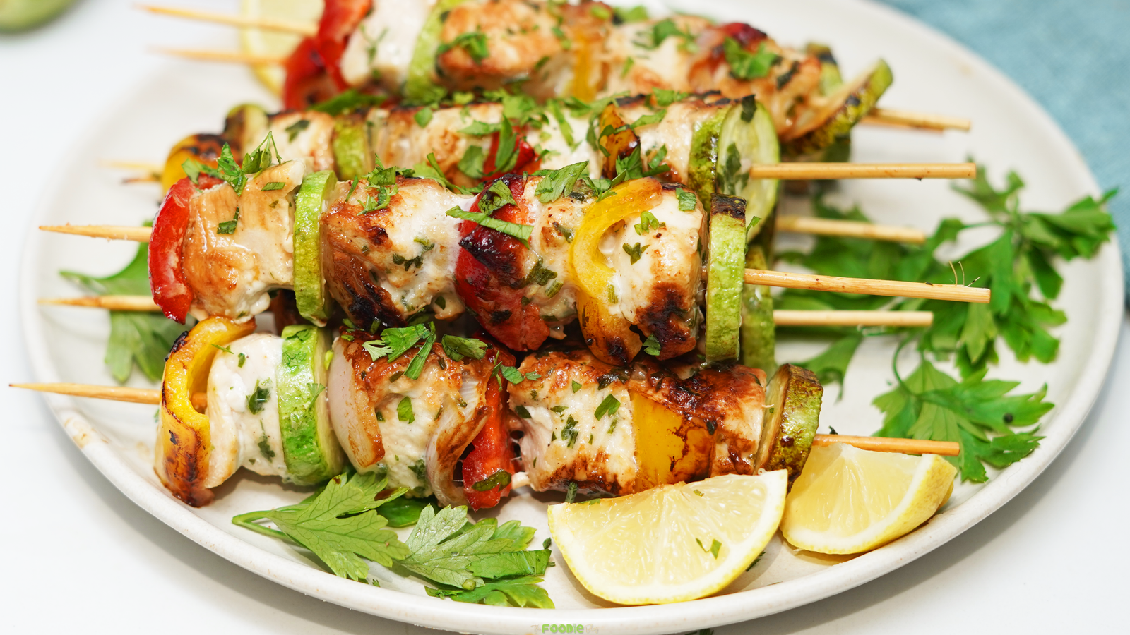Chicken Kabobs served on a plate with grilled vegetables, fresh parsley, and lemon wedges.