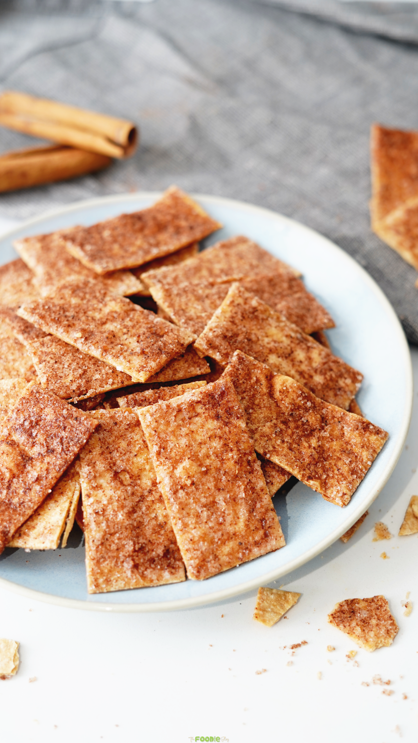 Golden cinnamon sugar tortilla crisps piled on a light blue plate with cinnamon sticks in the background.