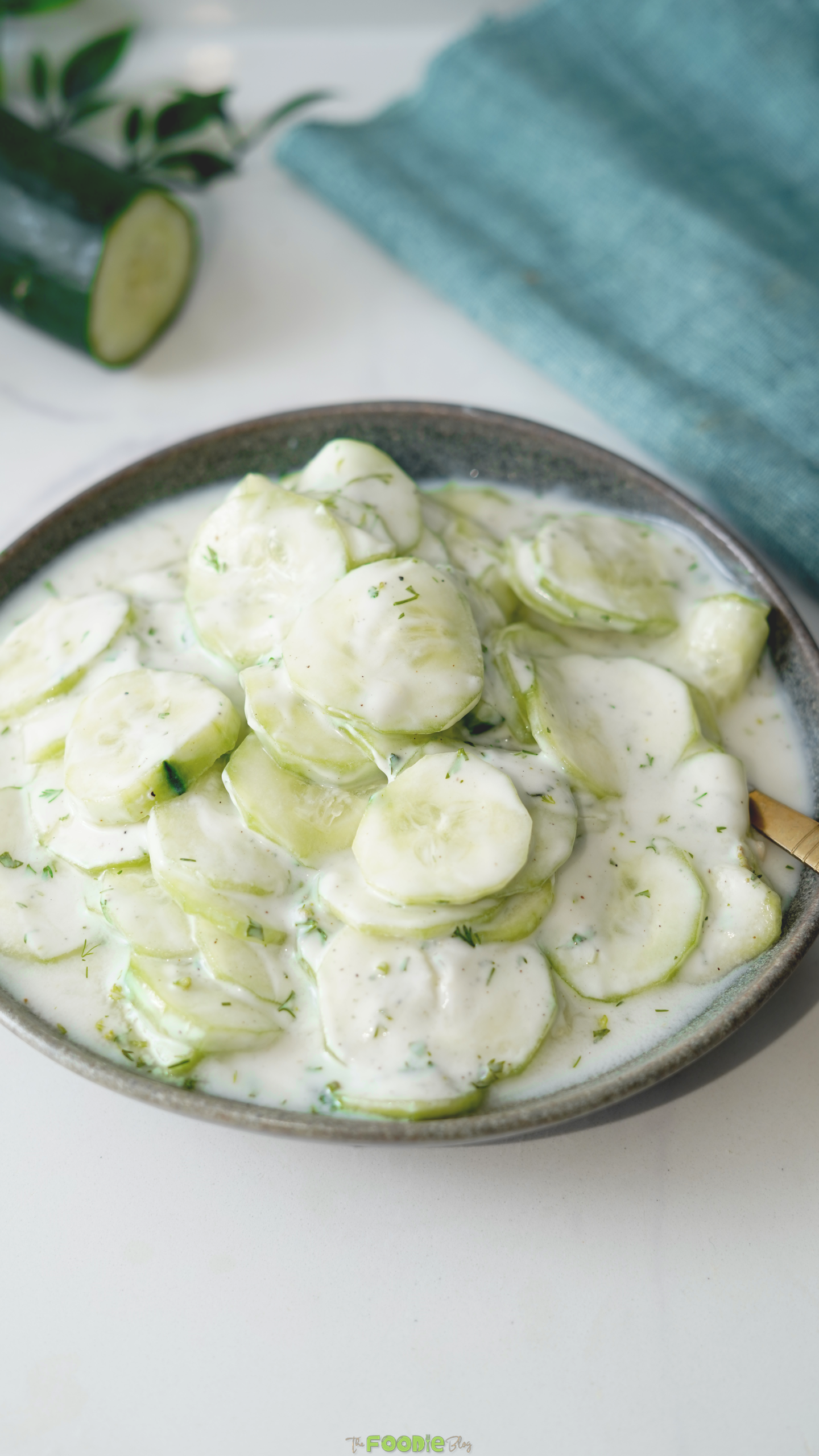Thin cucumber slices in a creamy sour cream and dill dressing in a gray serving bowl.