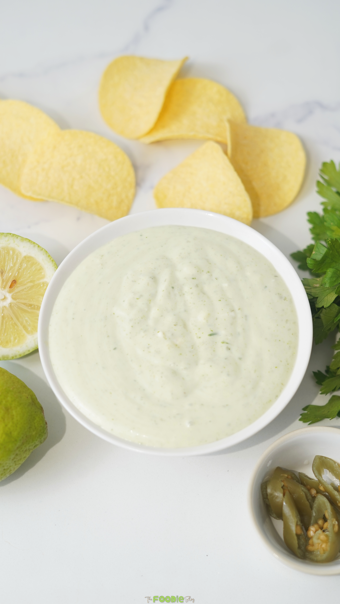 Chuy’s Creamy Jalapeno Copycat in a white bowl served with potato chips, lime, cilantro, and pickled jalapeños.