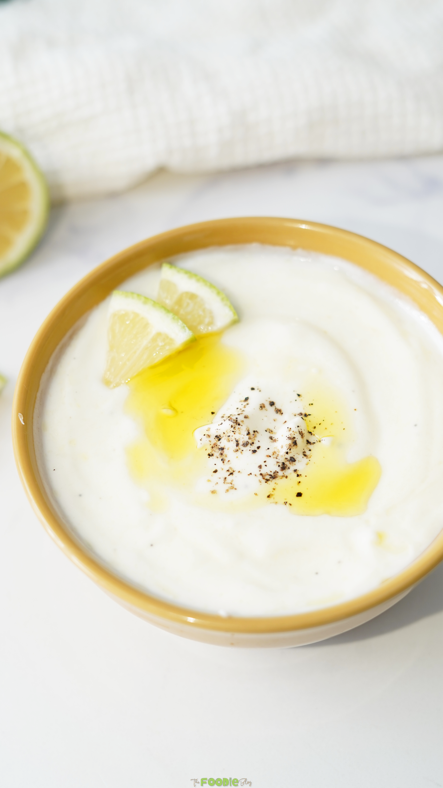 Creamy lemon yogurt sauce in a yellow bowl topped with olive oil, black pepper, and lemon wedges.