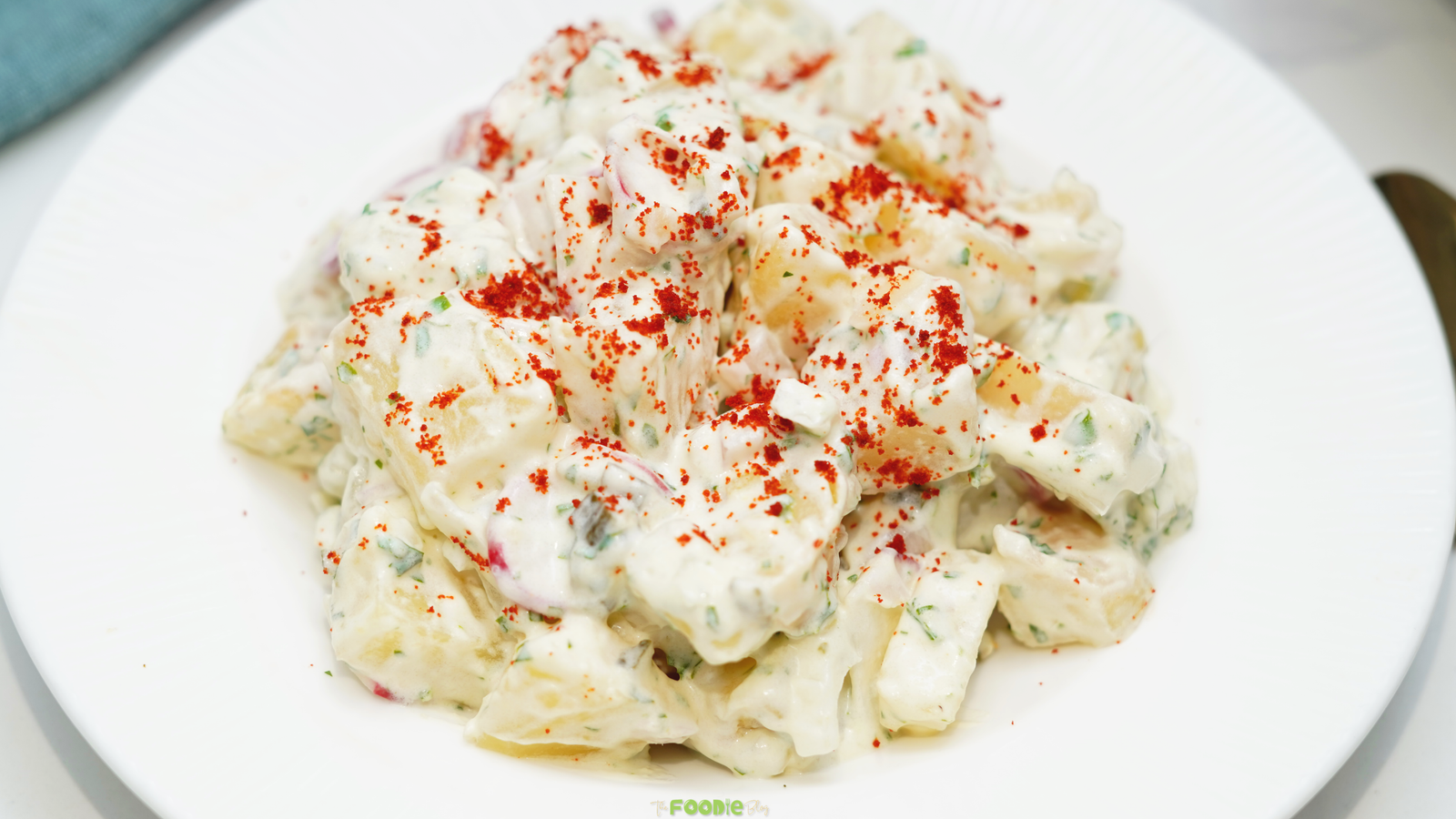 Creamy Potato Salad served on a white plate with paprika sprinkled on top.