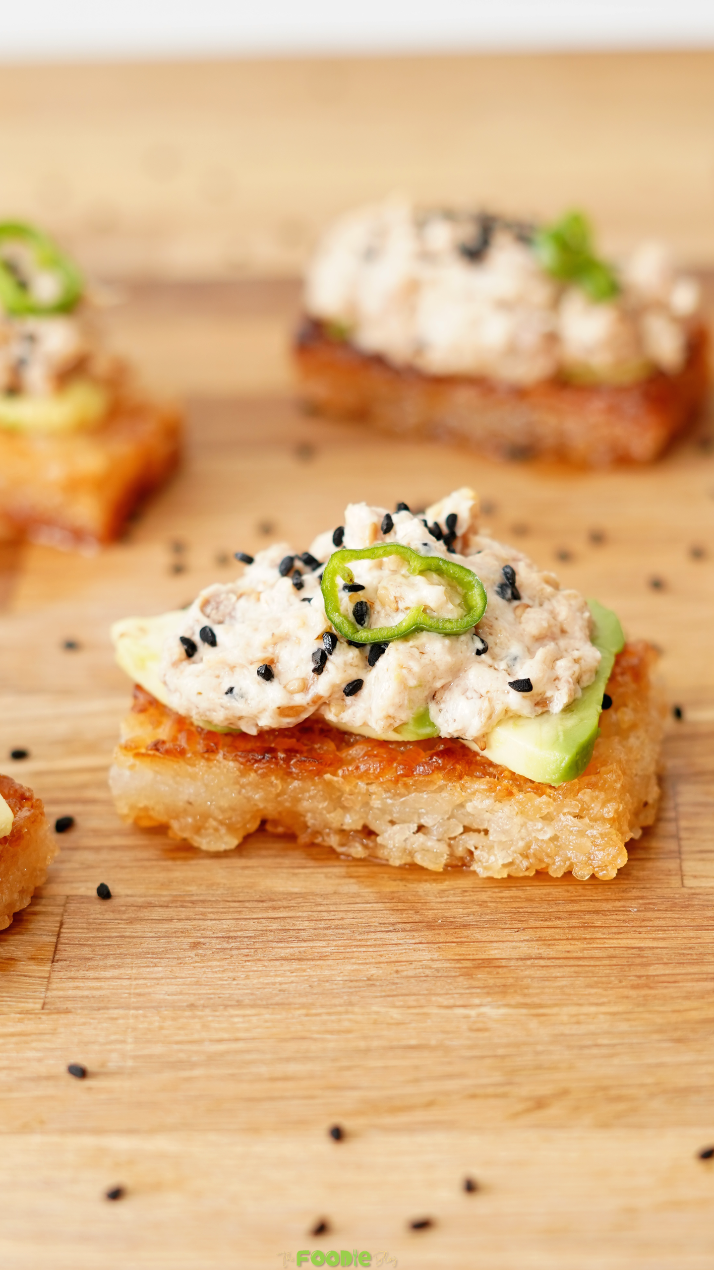 Close-up of crispy rice topped with avocado, creamy spicy tuna, black sesame seeds, and sliced jalapeño.