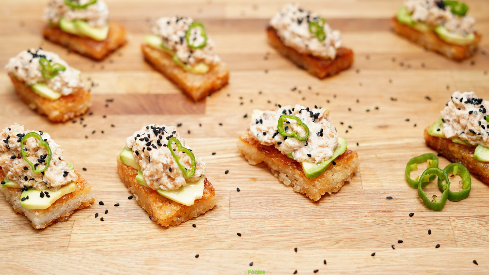 Crispy rice with spicy tuna, avocado, black sesame seeds, and sliced jalapeño arranged on a wooden serving board.