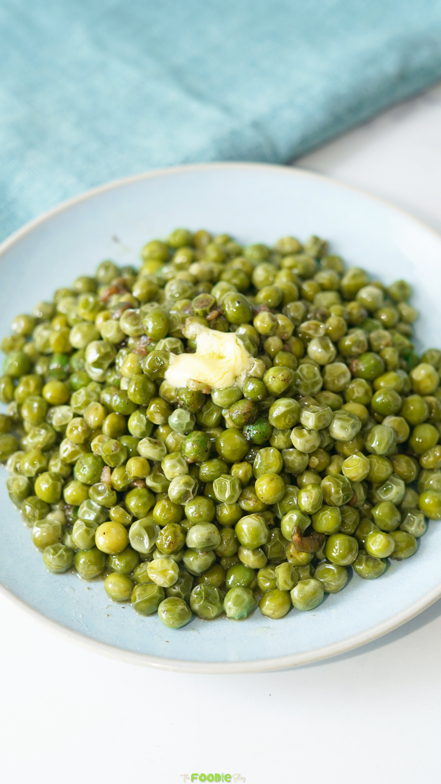 Garlic butter peas served on a pale blue plate beside a blue kitchen cloth