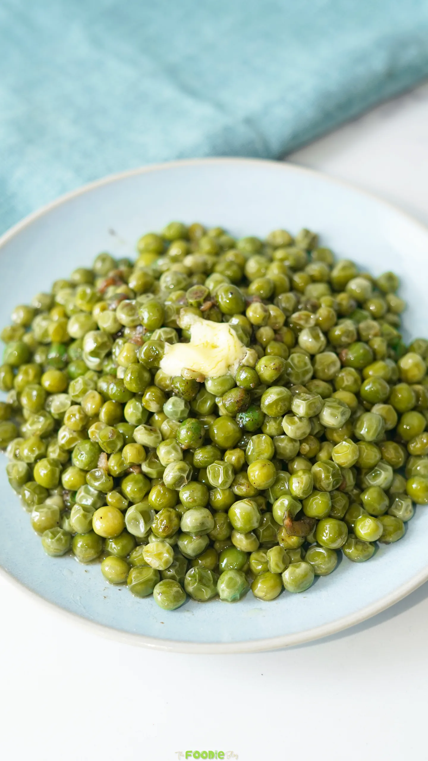 Garlic butter peas served on a pale blue plate beside a blue kitchen cloth